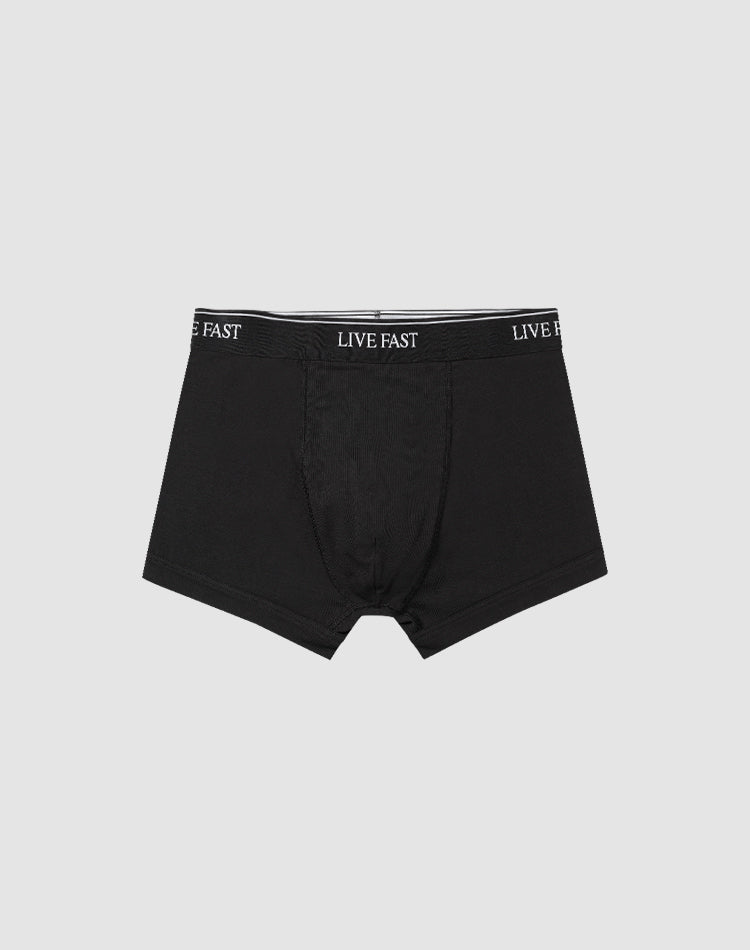 A pair of black Live Fast Trunks (2 Pack) by LIVE FAST DIE YOUNG, made from soft cotton with LIVE FAST repeatedly printed in white on the elastic waistband, displayed on a plain light gray background.