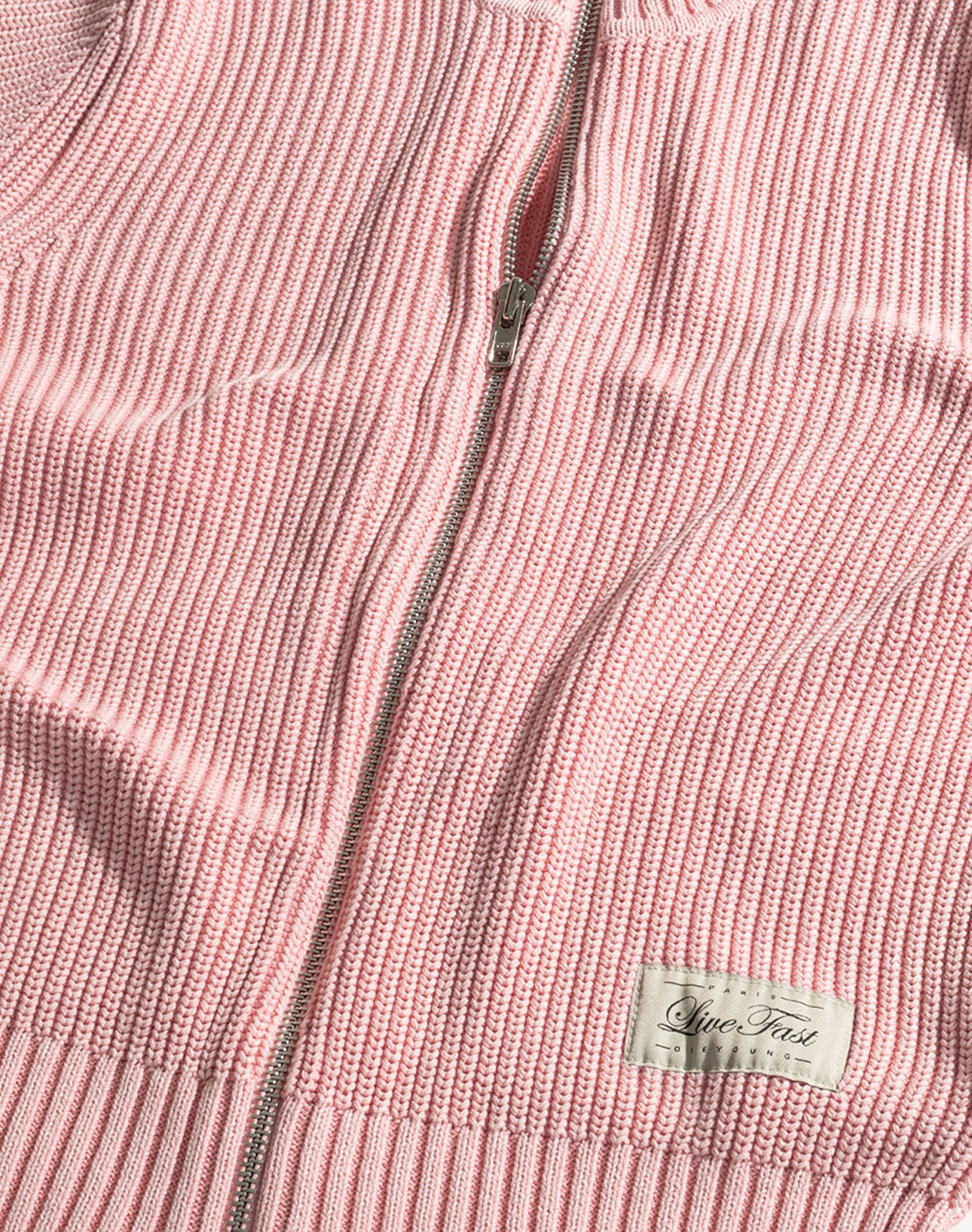 A close-up of the LFDY Knit Jacket by LIVE FAST DIE YOUNG in pink ribbed knit, featuring a zip-up front, Stehkragen, white "Live Fast" label at the hem, and made from 100% Baumwolle in a comfortable Regular Fit.
