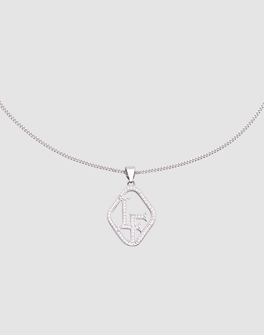 The LF Chain by LIVE FAST DIE YOUNG is a sterling silver necklace with a geometric pendant adorned with sparkling stones and stylized LF initials, featuring a zirconia charm, shown on a light gray background.