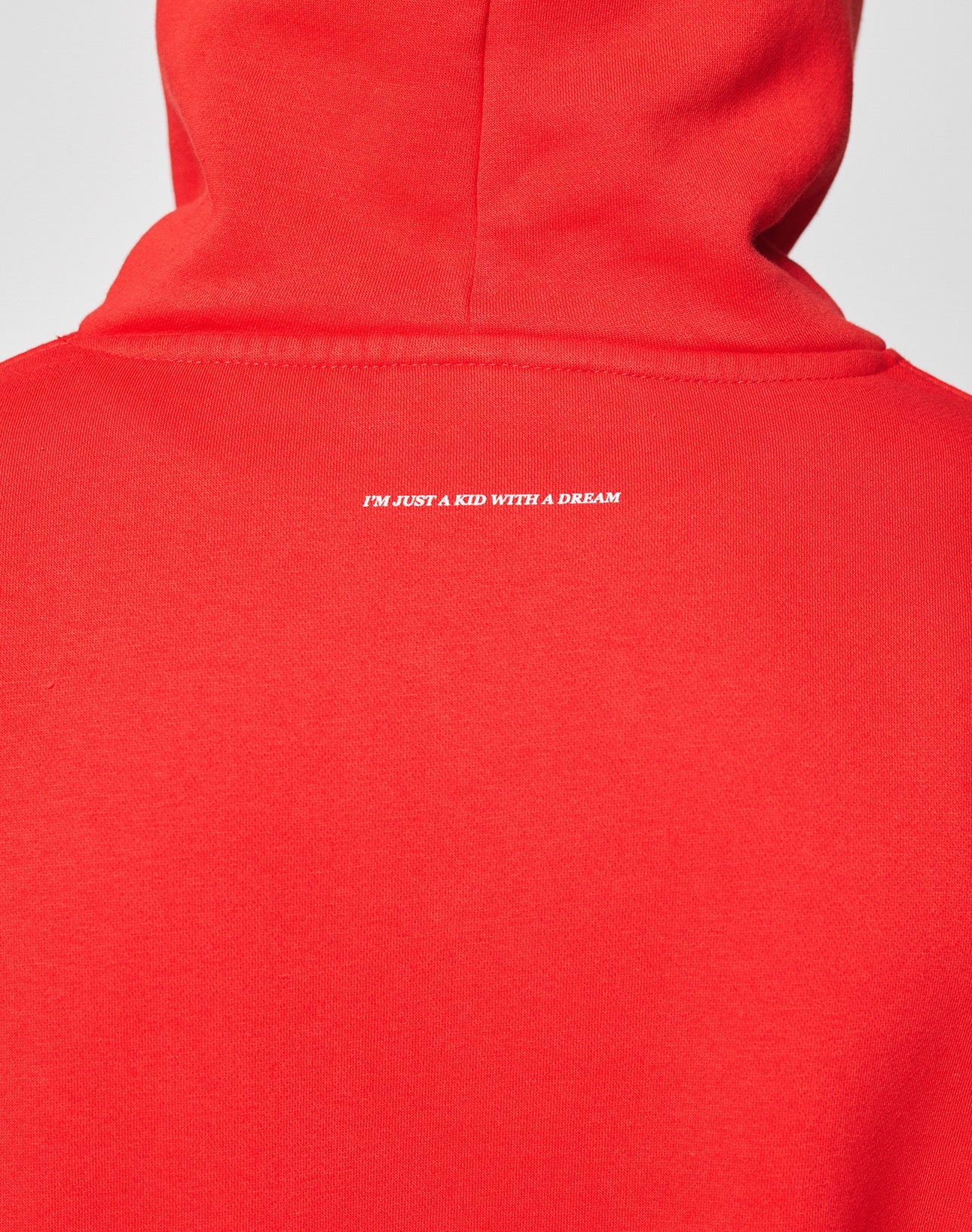 A person wearing an oversize fit, bright red Live Fast College Hooded by LIVE FAST DIE YOUNG, featuring a white IM JUST A KID WITH A DREAM backprint near the neck.