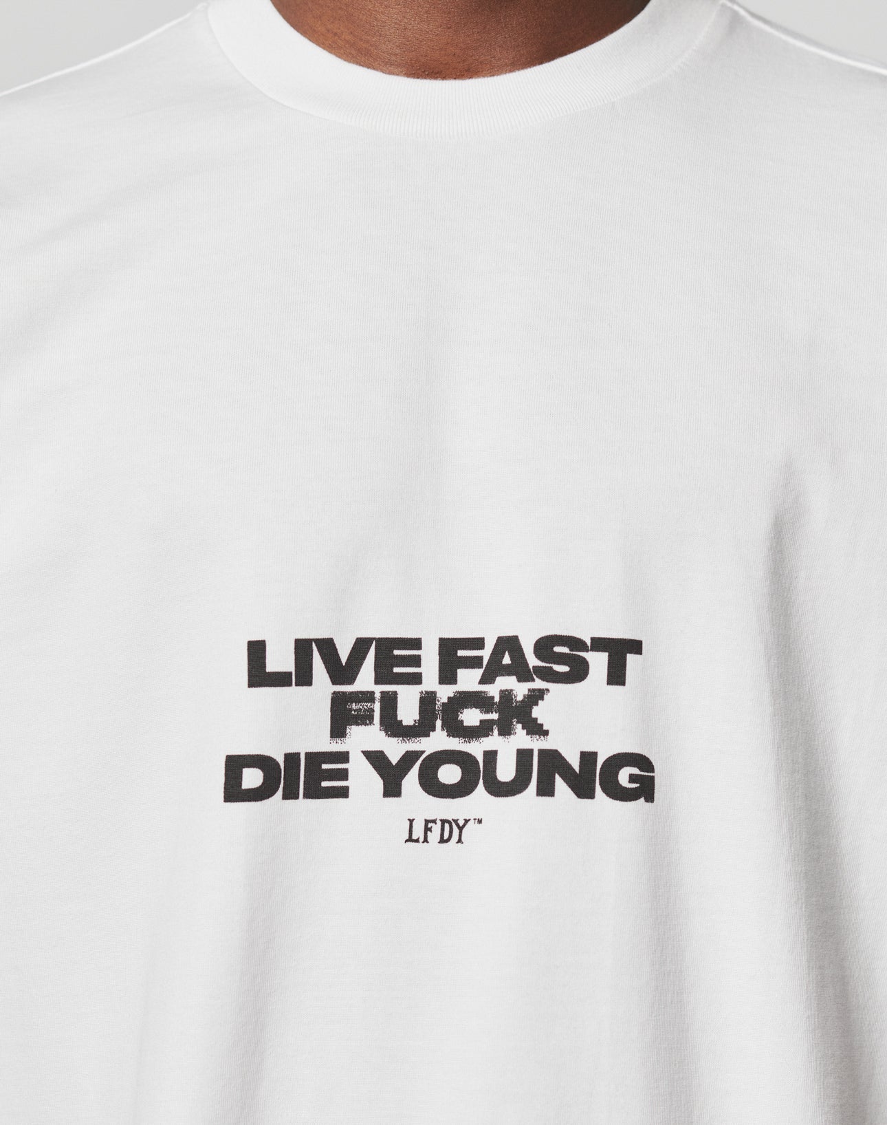 The Fuck Die Young Tee by LIVE FAST DIE YOUNG is a white oversized T-shirt featuring bold black “LIVE FAST FUCK DIE YOUNG” text and a smaller “LFDY” below, crafted from 100% Baumwolle for comfort and style.