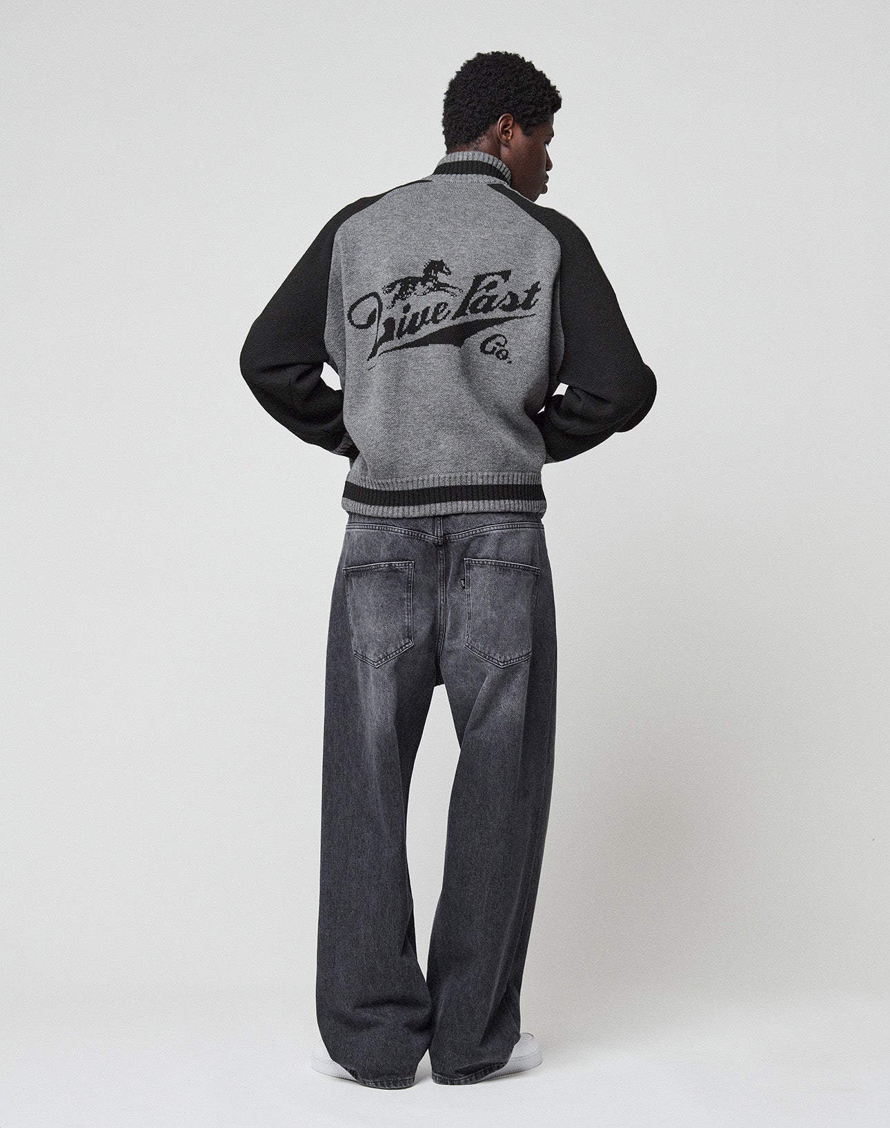 Close-up of gray fabric on the Boxy Knit Zip Jacket by LIVE FAST DIE YOUNG featuring raglan sleeves and a black galloping horse graphic above stylized "Live Fast" text.