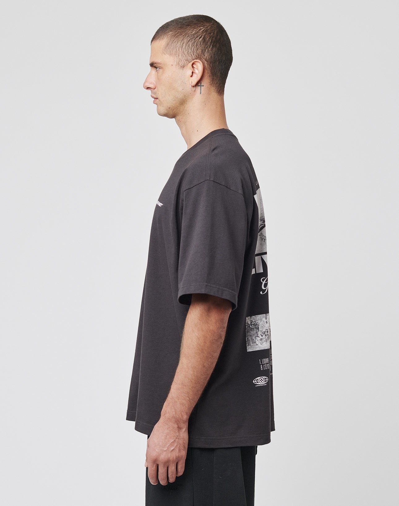 A man with short hair, wearing a loose-fitting LIVE FAST DIE YOUNG LFDY Cinema Tee and black pants, stands in profile against a plain white background.