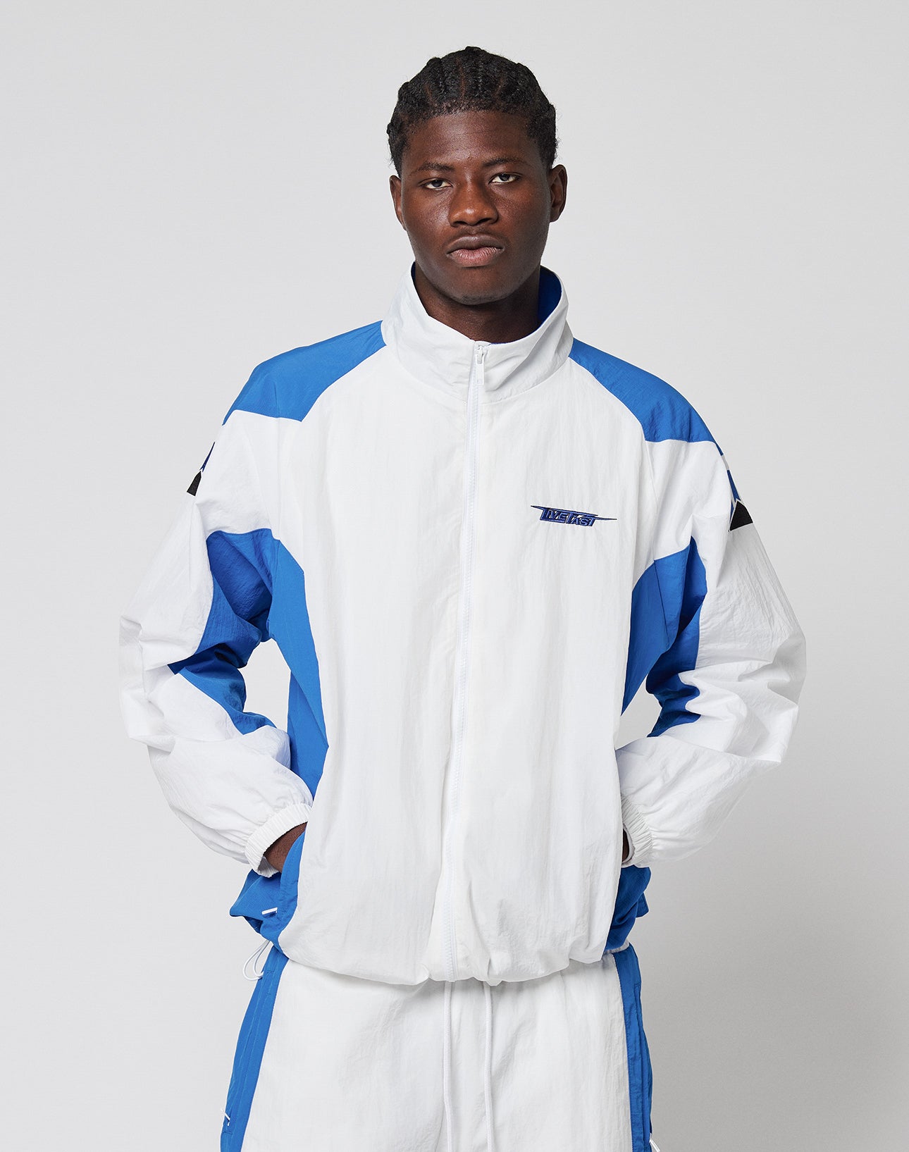 A person with a neutral expression stands against a plain background, wearing the LIVE FAST DIE YOUNG LFDY Trackjacket 3000 and matching track pants, hands in jacket pockets.