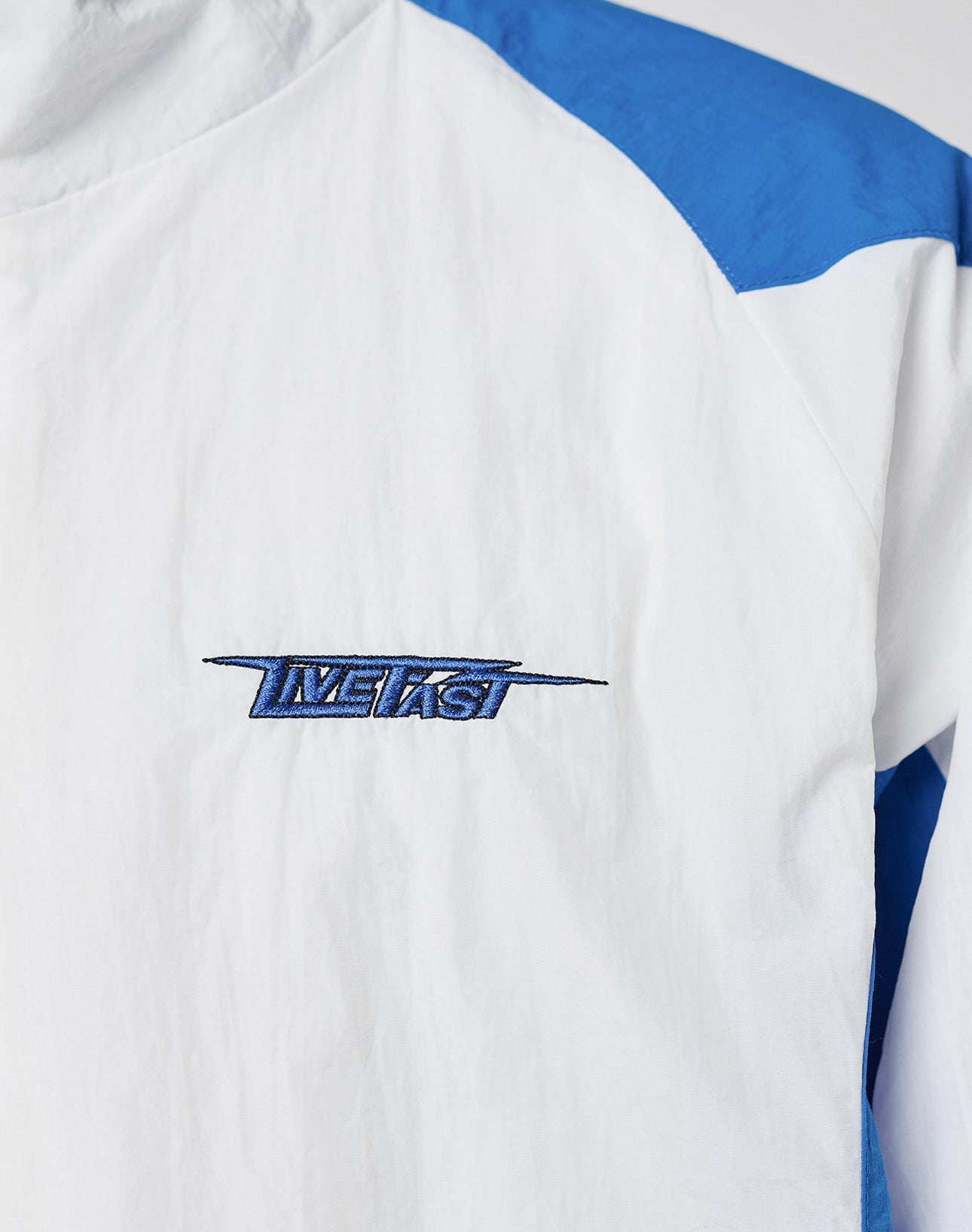 A close-up of the LFDY Trackjacket 3000 by LIVE FAST DIE YOUNG, featuring a white and blue polyamide design with the brand’s multilogo embroidered in blue on the chest.