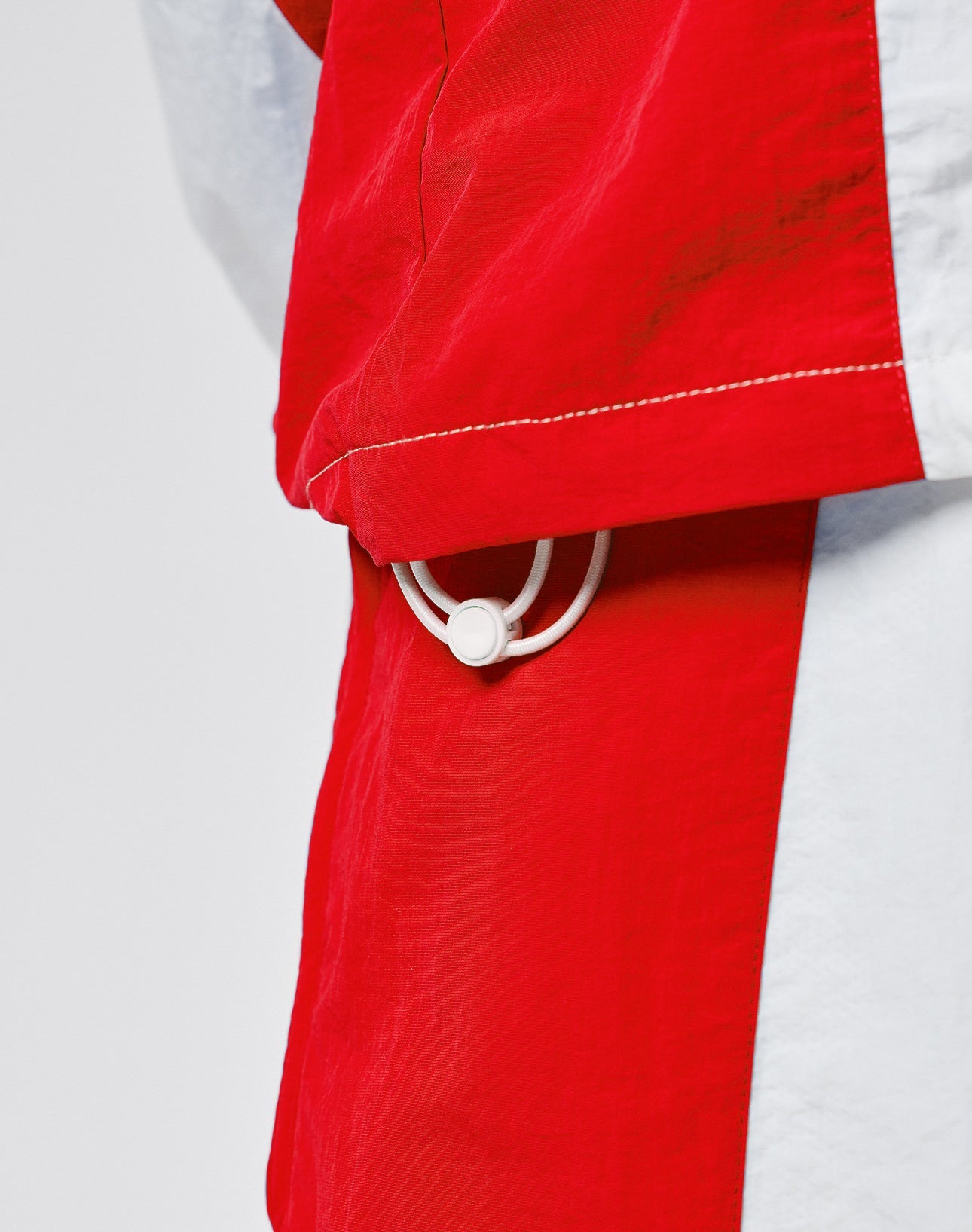 A close-up of the red and white LFDY Trackjacket 3000 by LIVE FAST DIE YOUNG, showing a white elastic drawstring loop with plastic adjuster at the hem and a branded zipper puller, set against a neutral blurred background.
