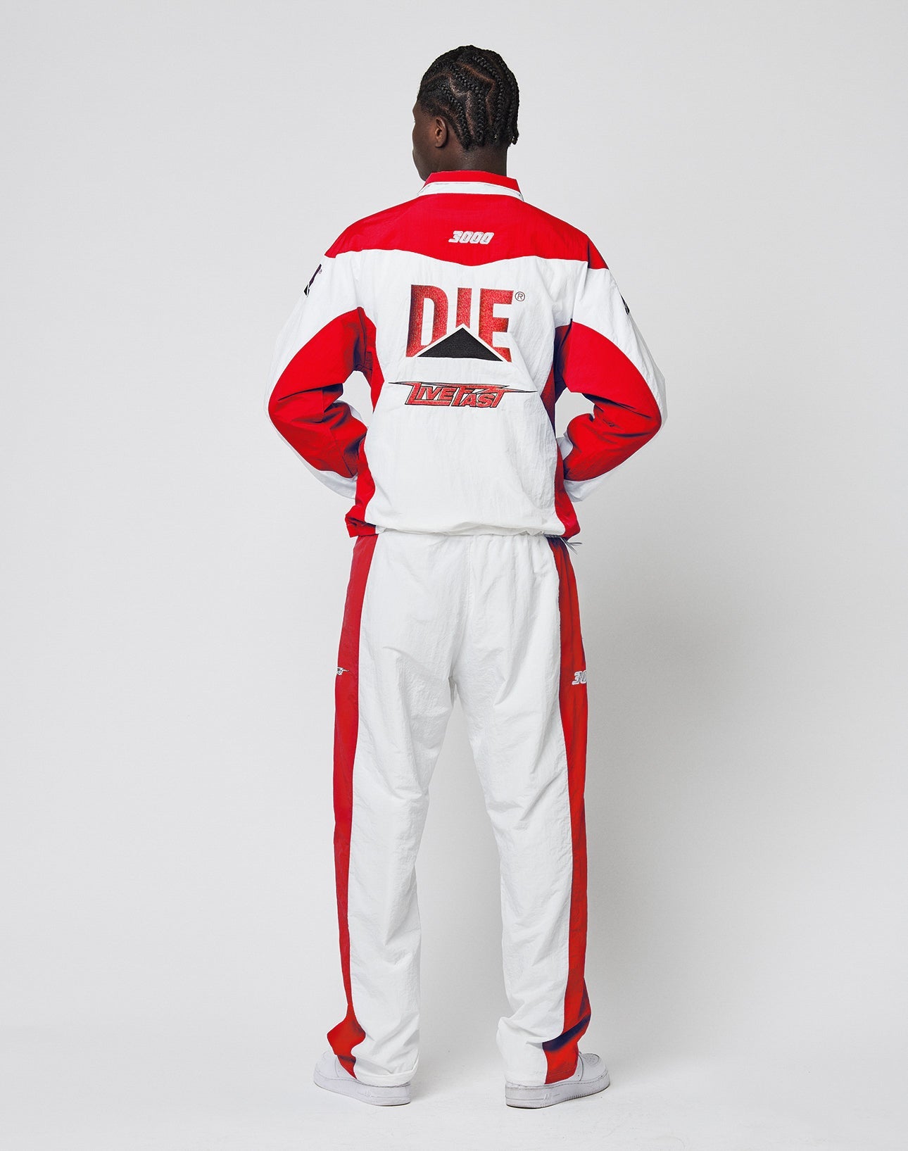 A person faces away in the LFDY Trackjacket 3000 by LIVE FAST DIE YOUNG, a regular fit tracksuit with bold red, white, and black color blocks, multilogo stick detailing, matching pants, and DIE/TV RACE printed on the back against a white background.