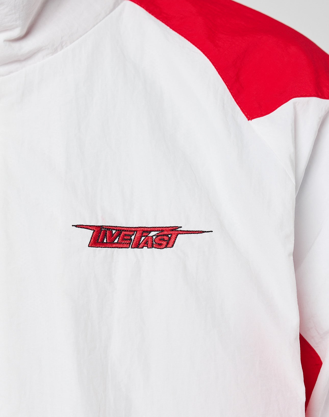 The LFDY Trackjacket 3000 by LIVE FAST DIE YOUNG is a white jacket with red shoulder panels, a branded zip puller, and an embroidered red and blue LIVE FAST logo on the chest. Regular fit for everyday comfort.