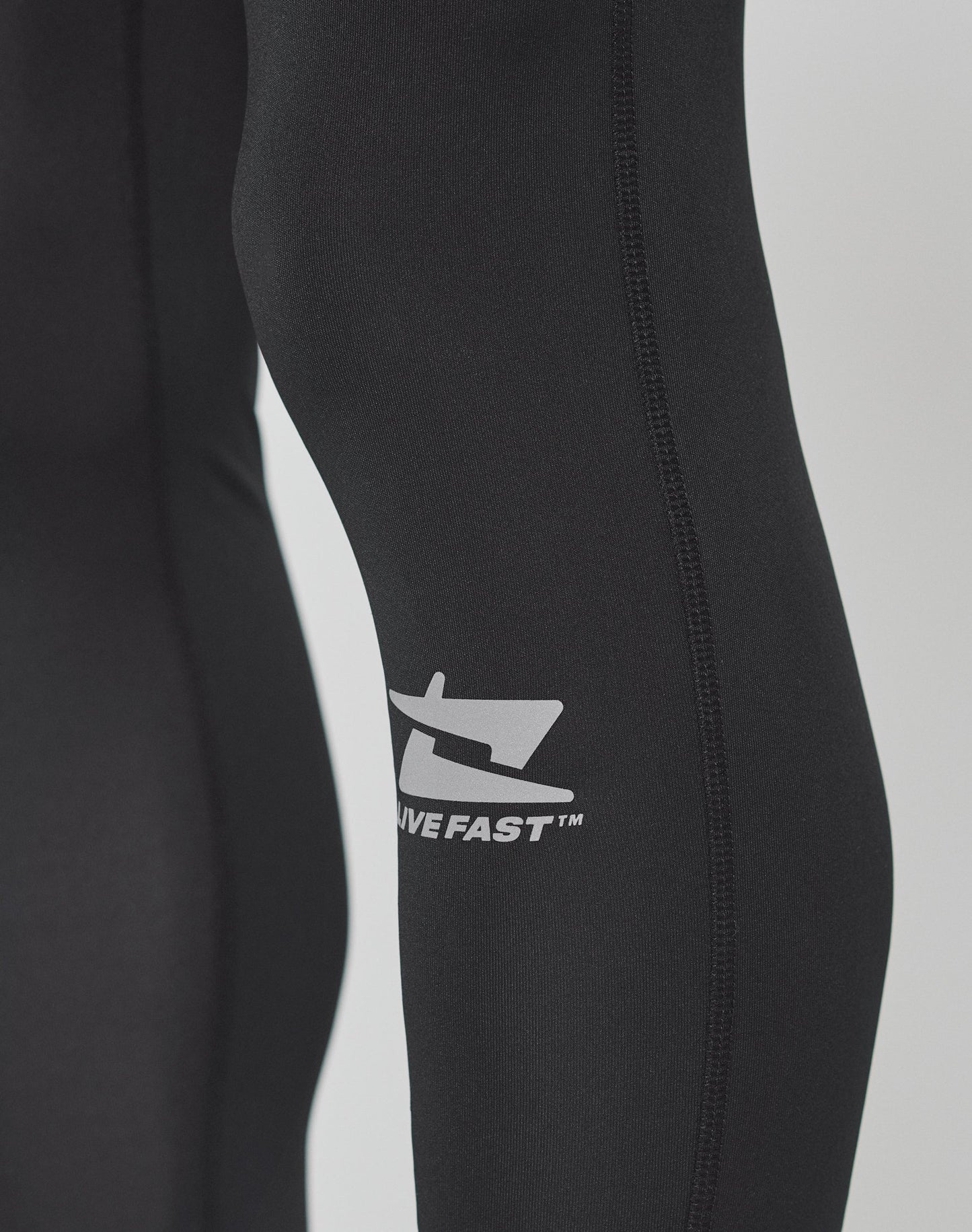 Close-up of a person wearing LIVE FAST DIE YOUNG Live Fast Performance Tights in black, featuring a white logo, DIVE FAST™ printed on the side, and a comfortable Elastikbund for added support.