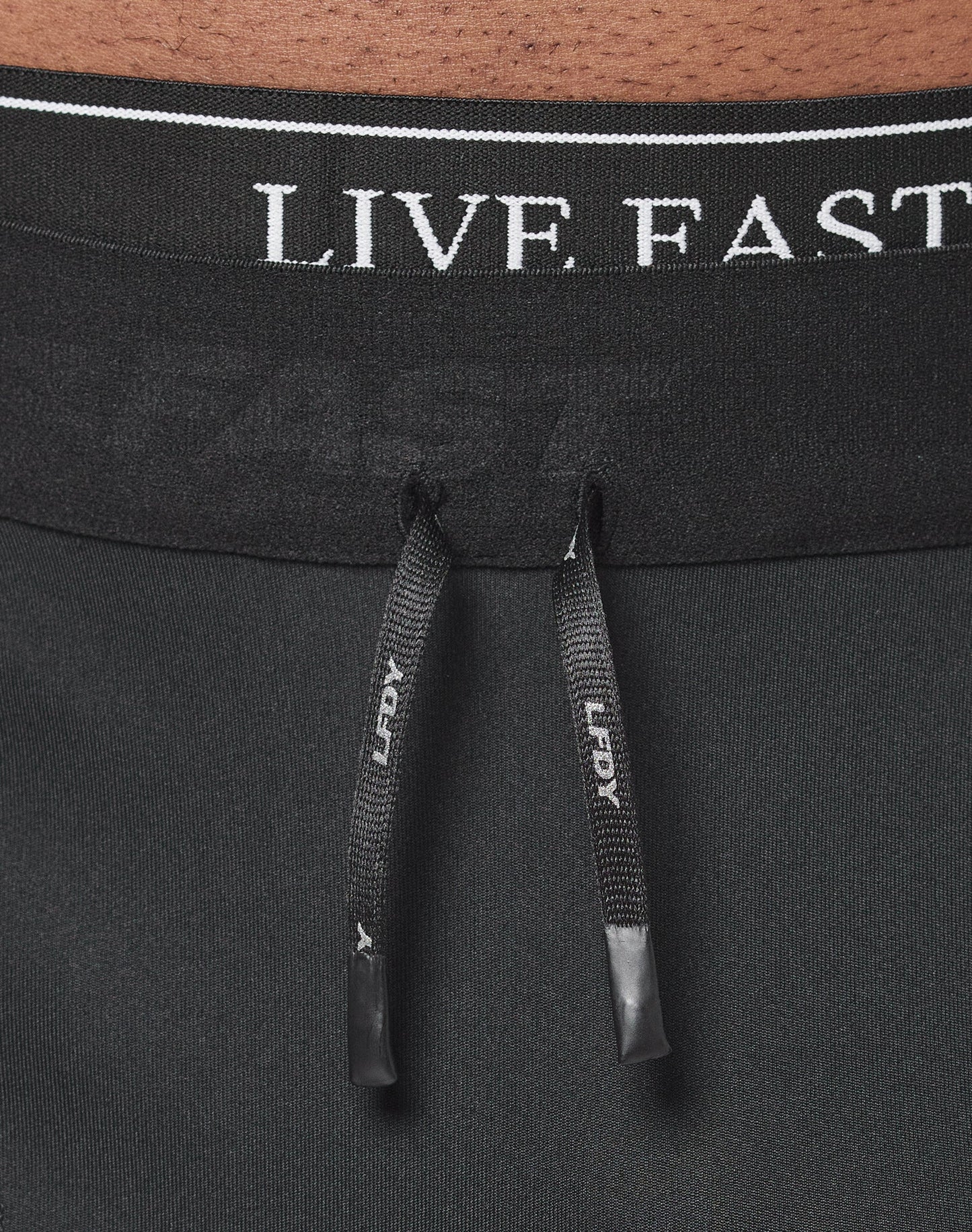 Close-up of the waistband on black Live Fast Performance Tights by LIVE FAST DIE YOUNG, featuring a comfortable Elastikbund, two black drawstrings with LEGACY in white, and partially visible Live Fast branding.