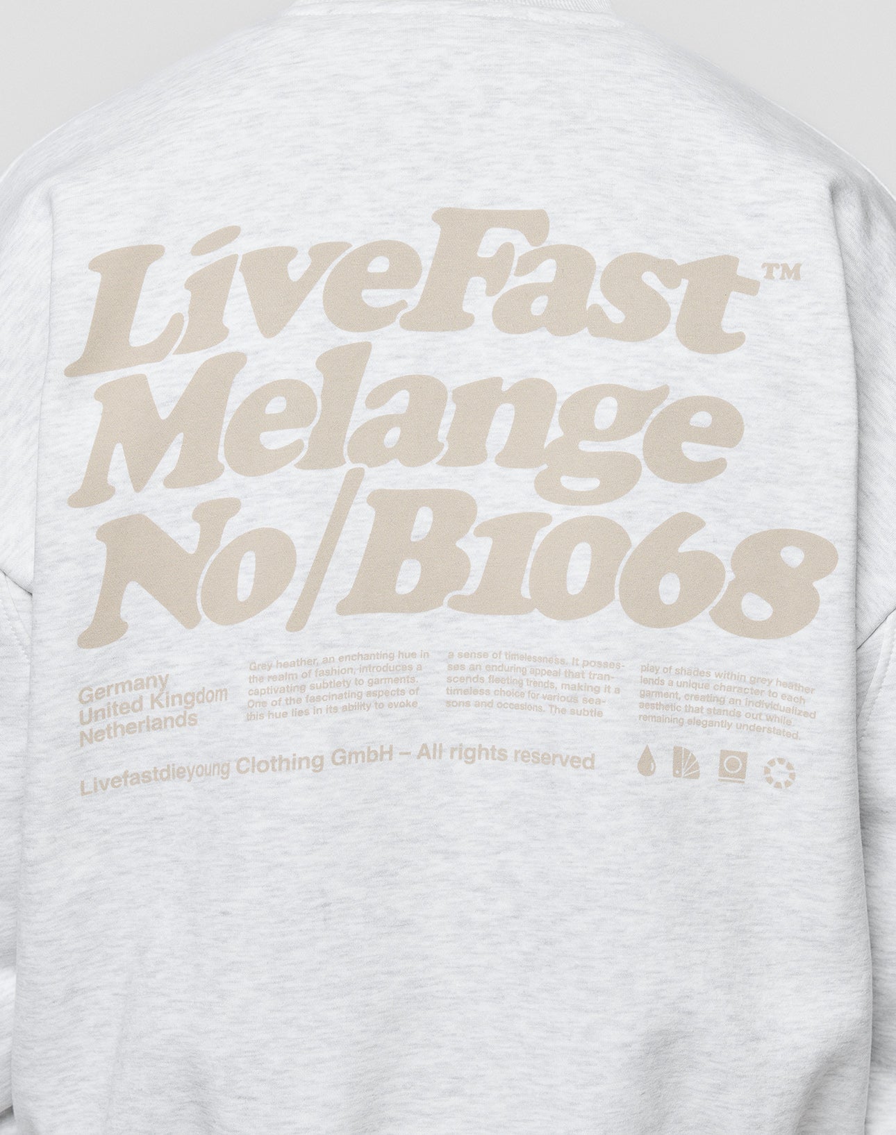 Back of a light gray Basic Melange Sweater by LIVE FAST DIE YOUNG features large beige “LiveFast Melange No/B1068” text, smaller text listing Germany, United Kingdom, Netherlands, and branding at the bottom. Made from soft Baumwolle.