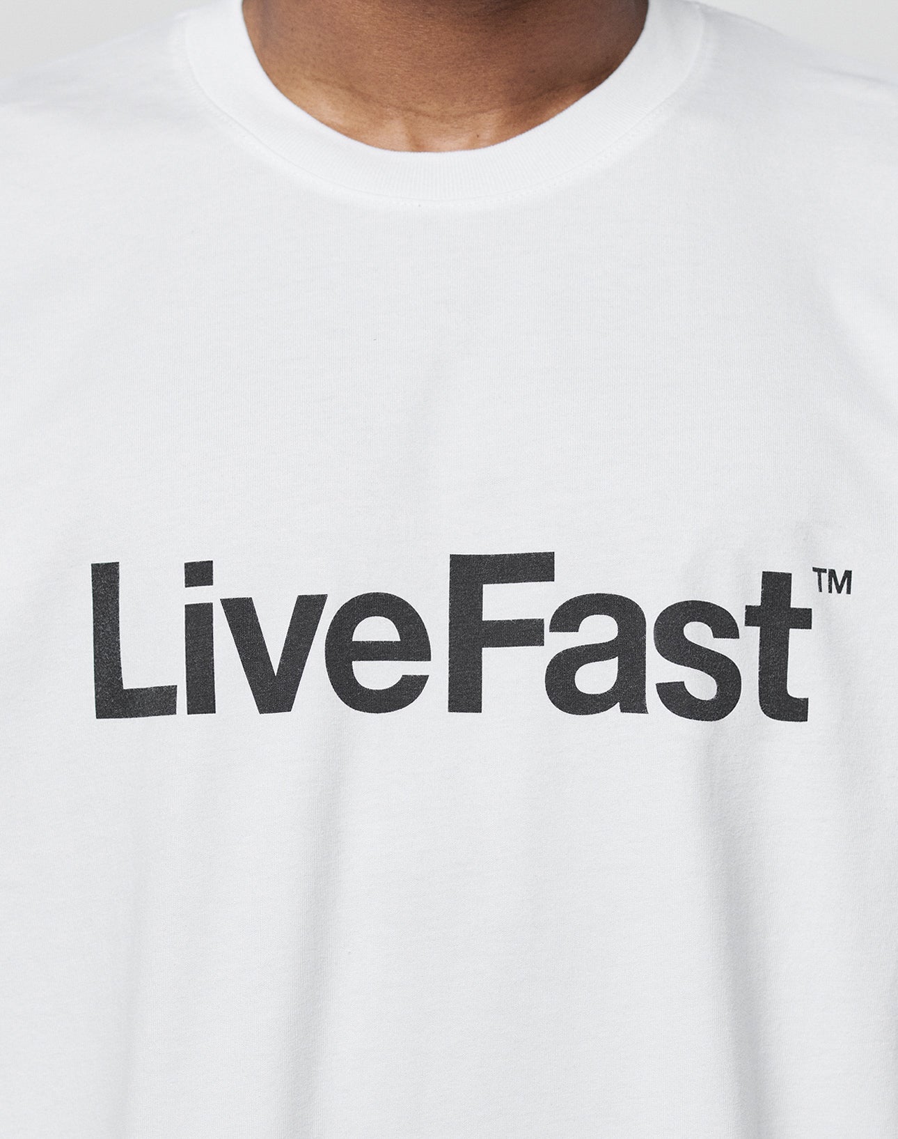 A person wears the Basic LiveFast Tee by LIVE FAST DIE YOUNG—white, regular fit, cotton t-shirt with “LiveFast™” printed in bold black letters across the chest.