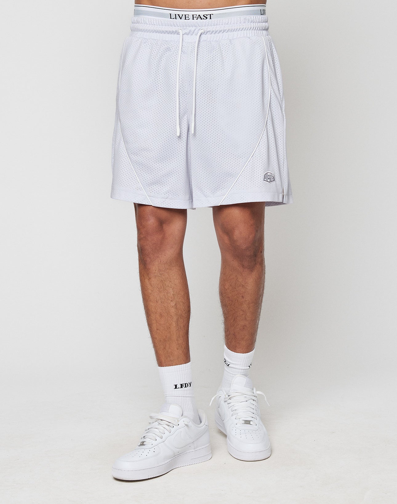 A person in regular fit LFDY Piping Mesh Shorts by LIVE FAST DIE YOUNG, white LDYY socks, white sneakers, and polyester underwear with a LIVE FAST waistband stands against a plain white background.