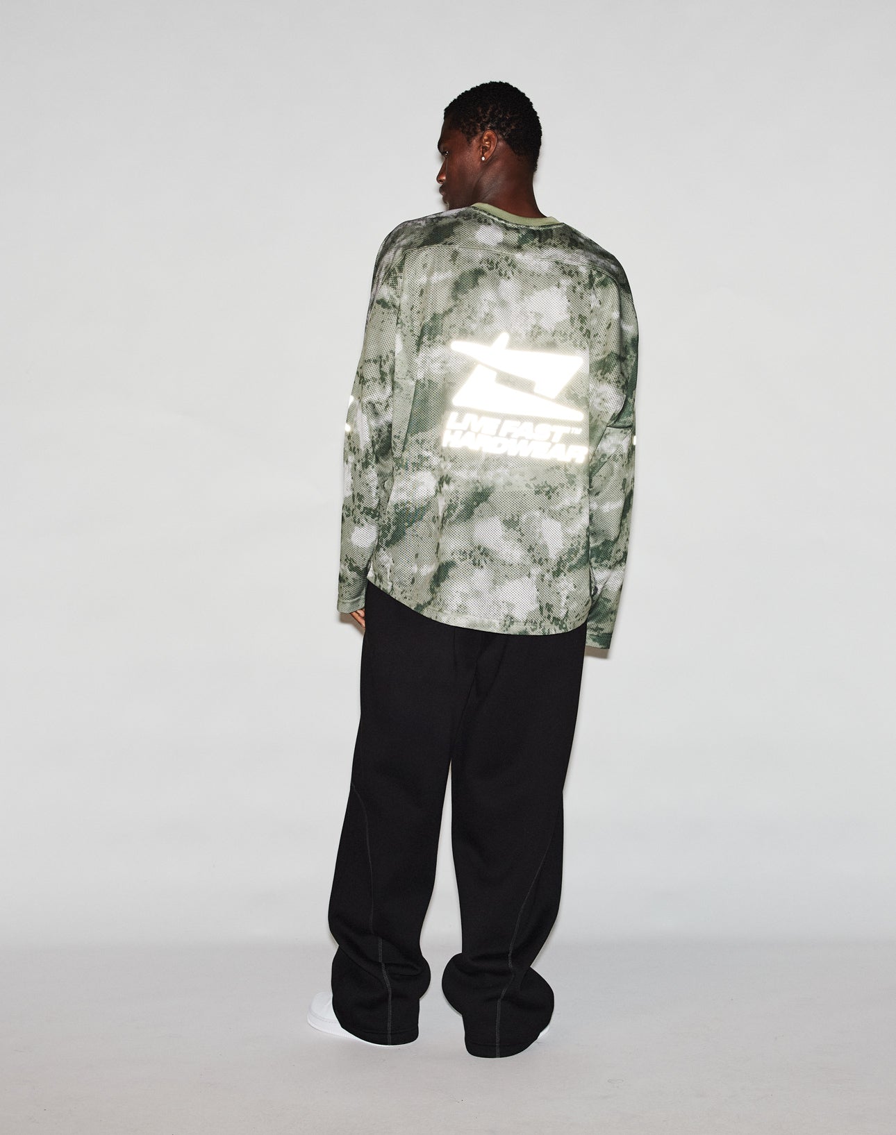 A person stands facing away, wearing the LIVE FAST DIE YOUNG Camo Mesh Jersey and black pants, set against a plain light background.