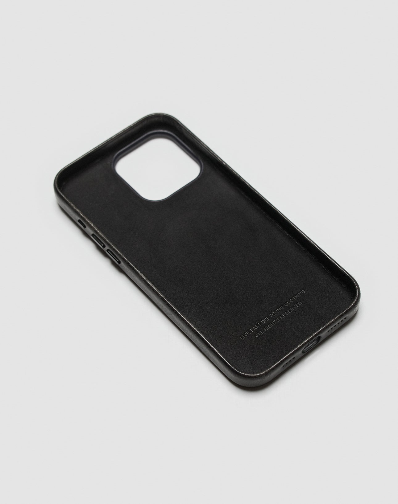 A black Live Fast Phone Case by LIVE FAST DIE YOUNG rests on a light gray surface, angled to display its interior, side button cutouts, and embossed logo.