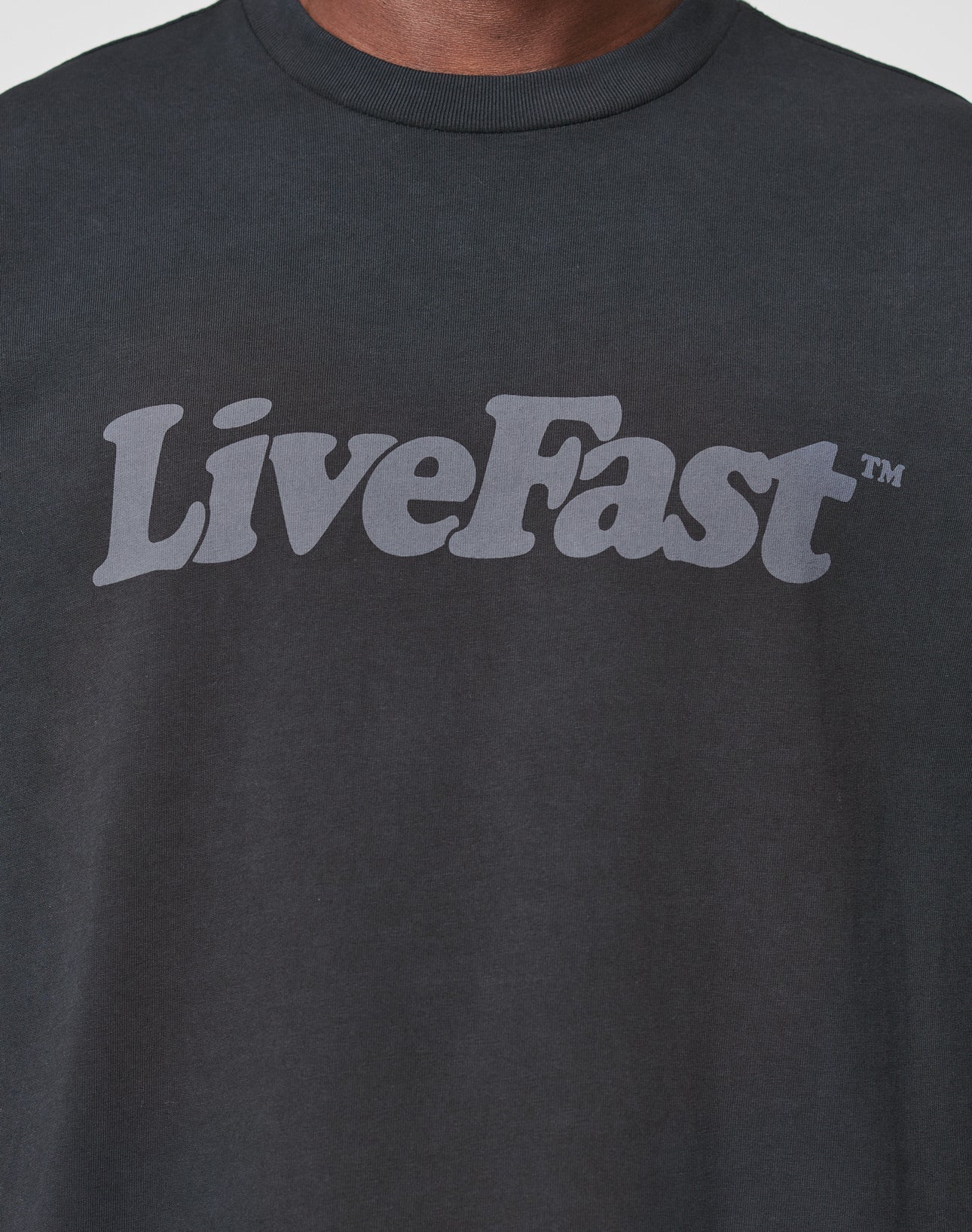 A close-up of the LIVE FAST DIE YOUNG Basic Tee, a black, oversized cotton shirt with LiveFast™ in bold light gray across the chest and a vintage-wash finish for standout style.