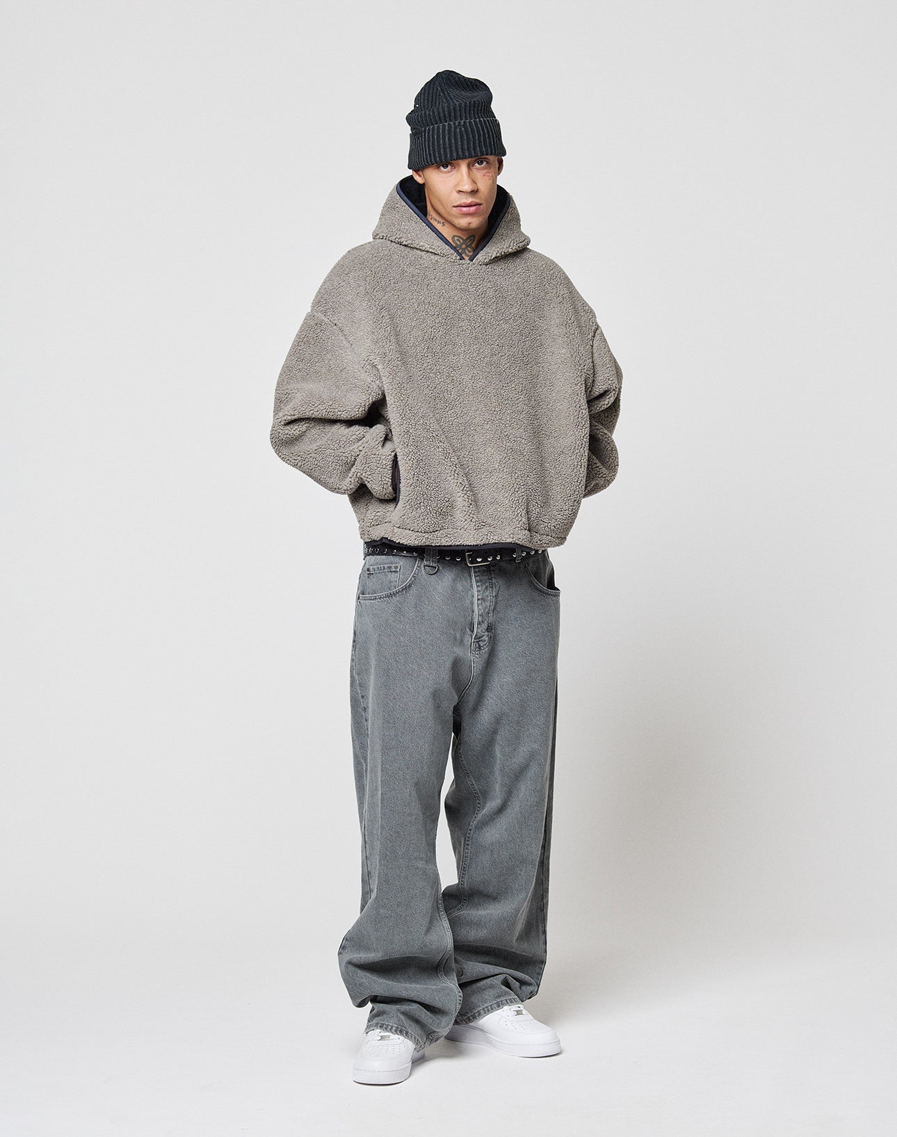 A person wears a loose gray hoodie, LIVE FAST DIE YOUNG LFDY Baggy Denim jeans, white sneakers, and a black knit beanie, standing against a plain light background with hands in their pockets.