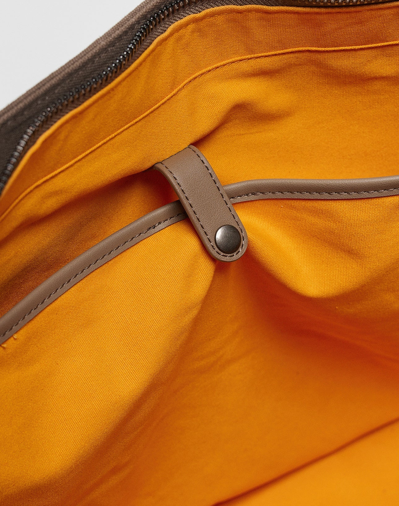 Close-up of the LFDY Tote Bag by LIVE FAST DIE YOUNG, featuring an orange fabric interior, a brown leather-trimmed pocket secured by a strap and snap button, a top zipper, and a dedicated laptop compartment.
