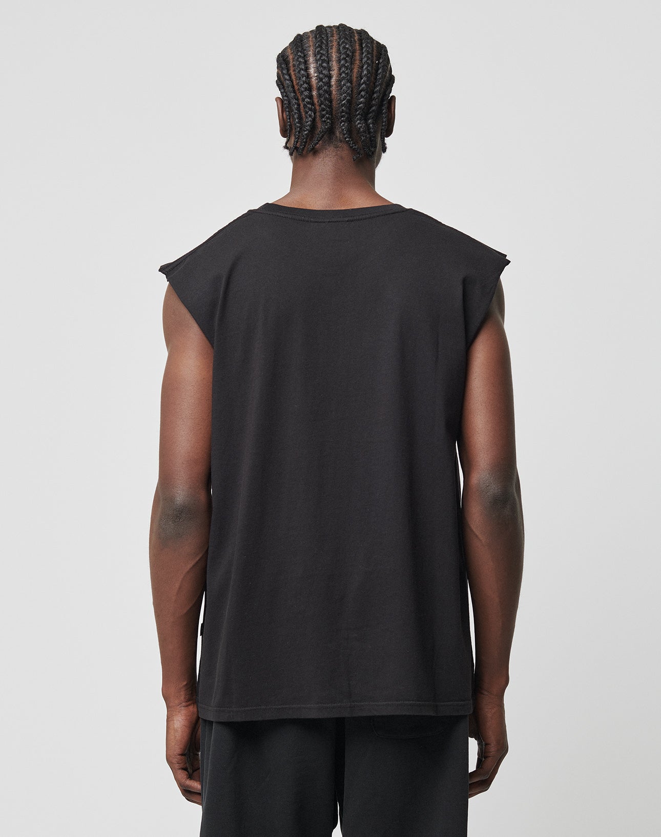 A person with braided hair, seen from behind, wears the LIVE FAST DIE YOUNG Basic Muscle Shirt aus 100% Baumwolle and black Loose Fit pants against a plain light background.
