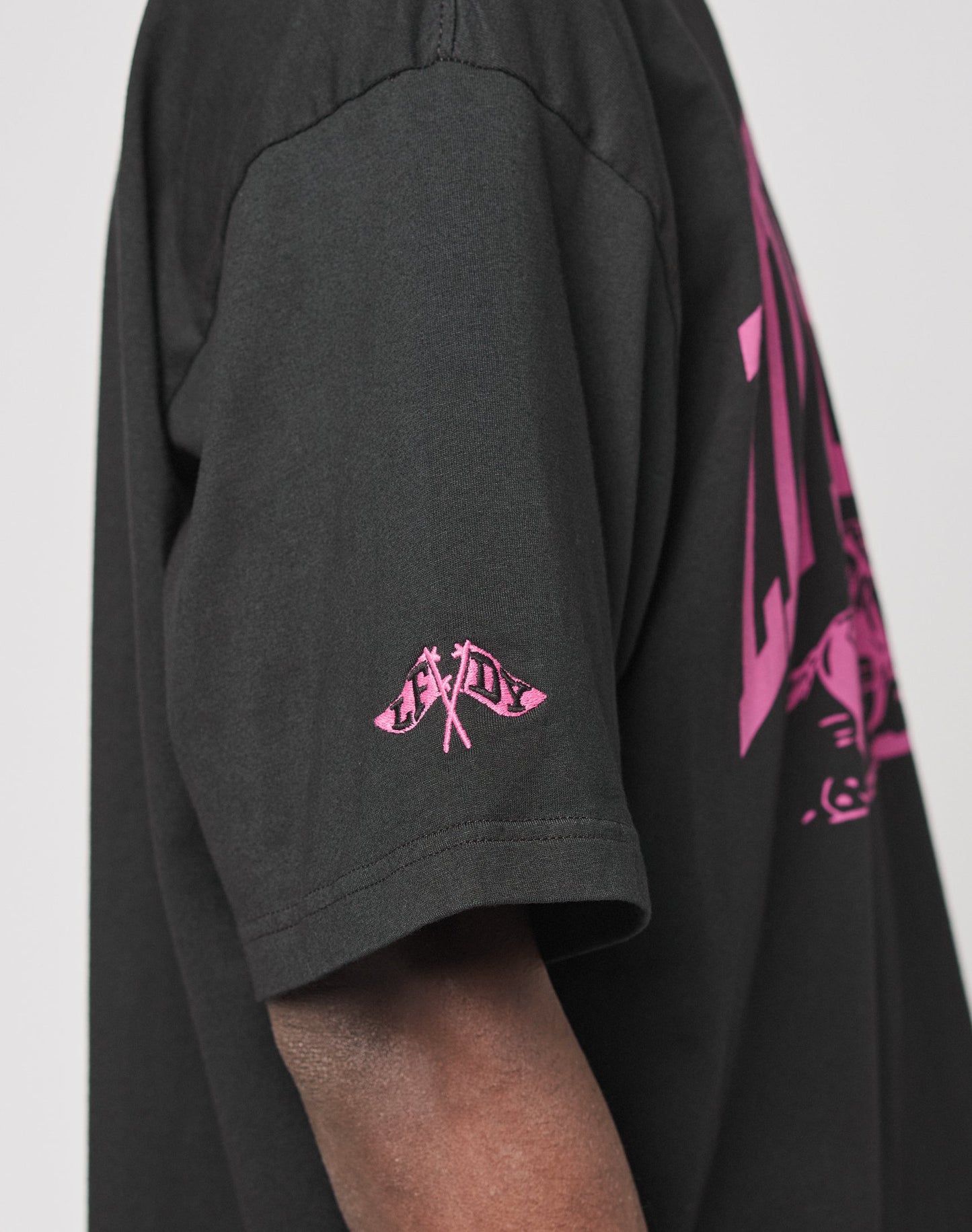 Someone wears the Live Fast Stallion Tee by LIVE FAST DIE YOUNG, a black oversized 100% Baumwolle T-shirt featuring a small pink crossed flags front print, LADY on the sleeve, and a larger pink back design.