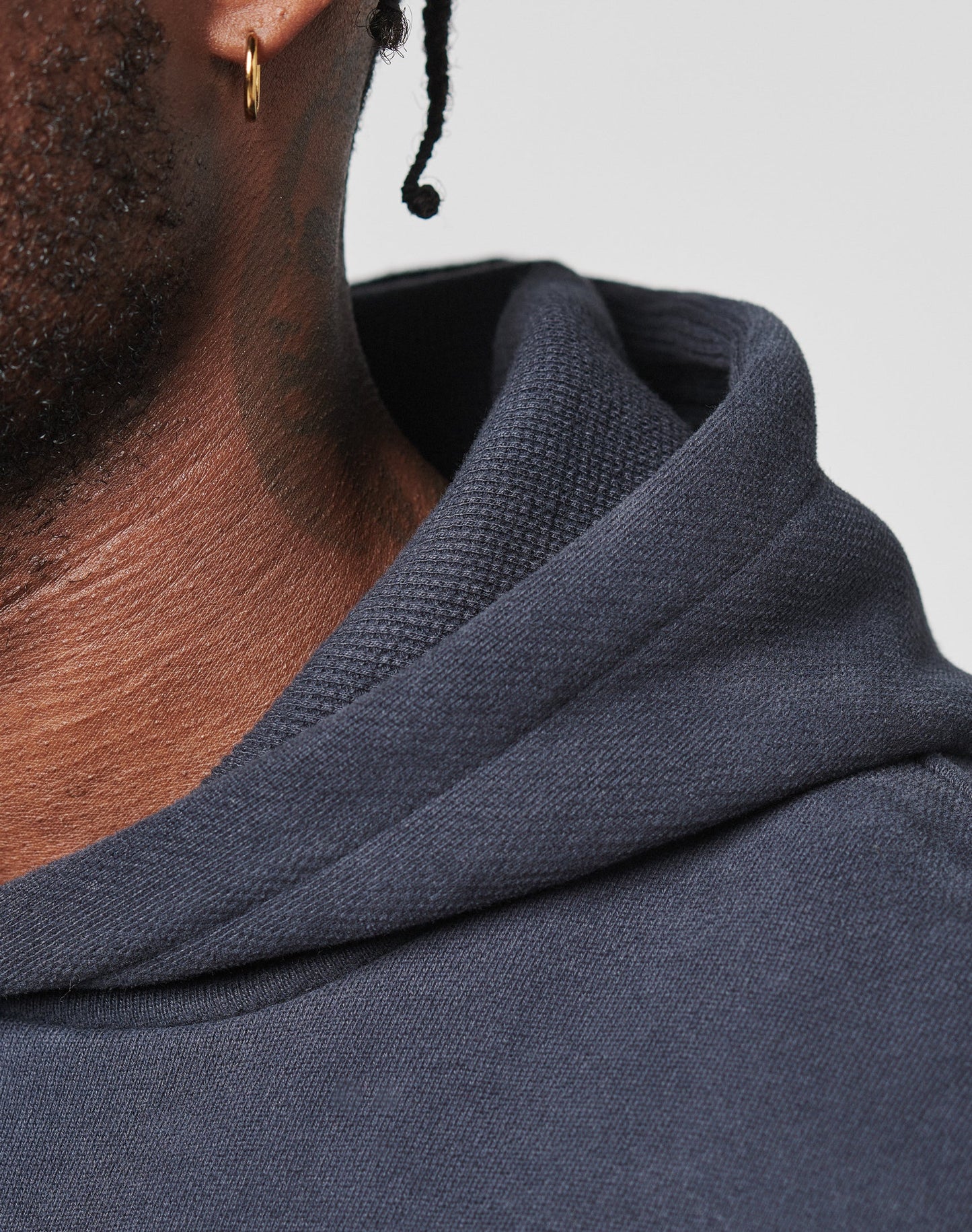 Close-up of a person with dark skin and a small braid, wearing a gold hoop earring and an oversized dark navy LFDY Script Hooded by LIVE FAST DIE YOUNG.