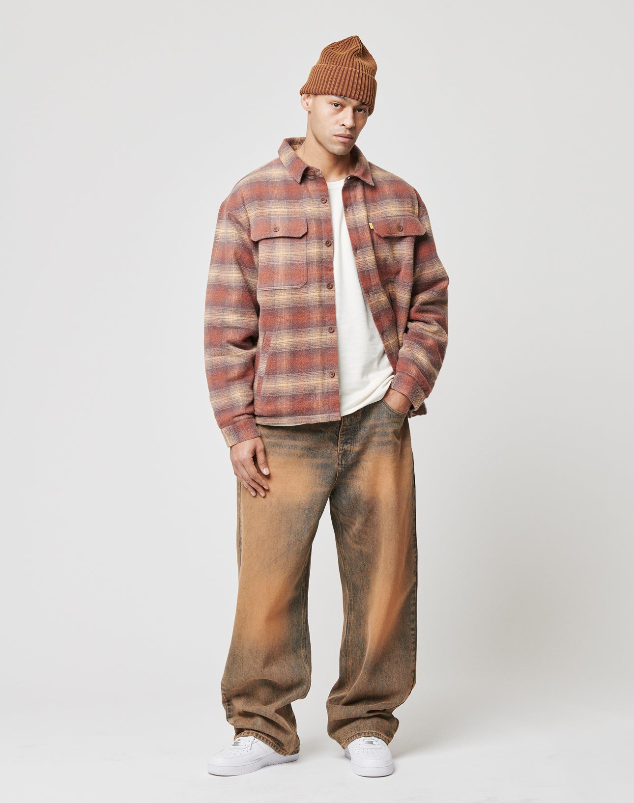 A man in a brown beanie, red and brown plaid jacket over a white shirt, LIVE FAST DIE YOUNG LFDY Baggy Denim jeans (100% cotton) and white sneakers stands against a plain white background.