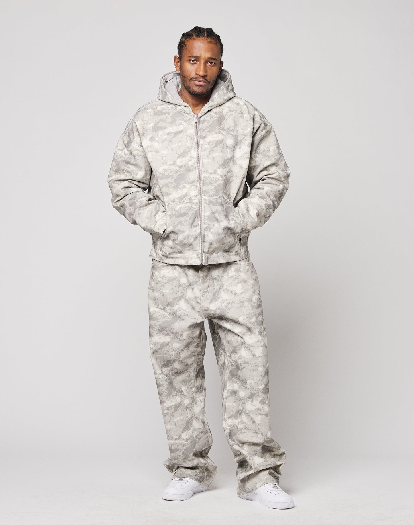 A man stands against a plain background wearing the Live Fast Canvas Jacket by LIVE FAST DIE YOUNG with his hands in his pockets, paired with matching pants and white sneakers.