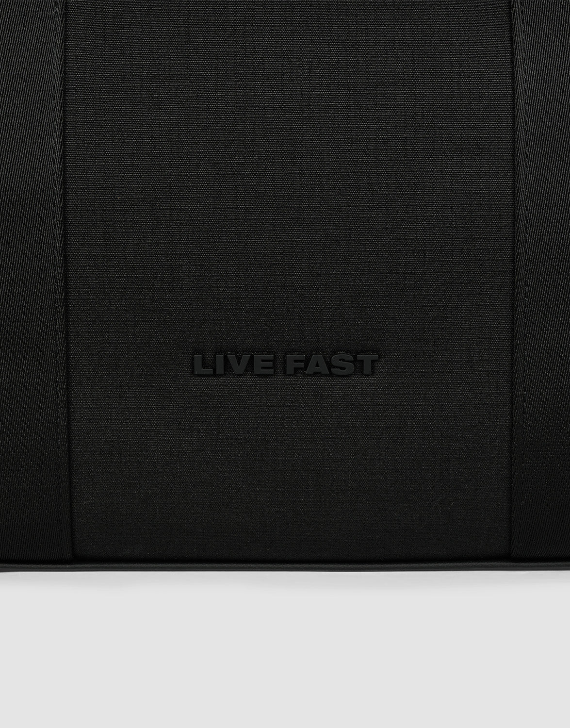 A close-up of black textured polyester from the LFDY Utility Bag by LIVE FAST DIE YOUNG, featuring "LIVE FAST" embossed in the center and hinting at its großes Fach for practical use.