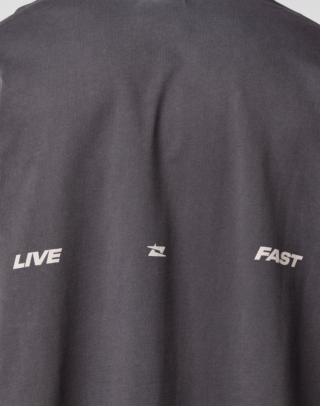 Close-up of the backprint on the dark gray Live Fast Cropped Oversized Tee by LIVE FAST DIE YOUNG, showing LIVE and FAST in white, separated by a small abstract white symbol.