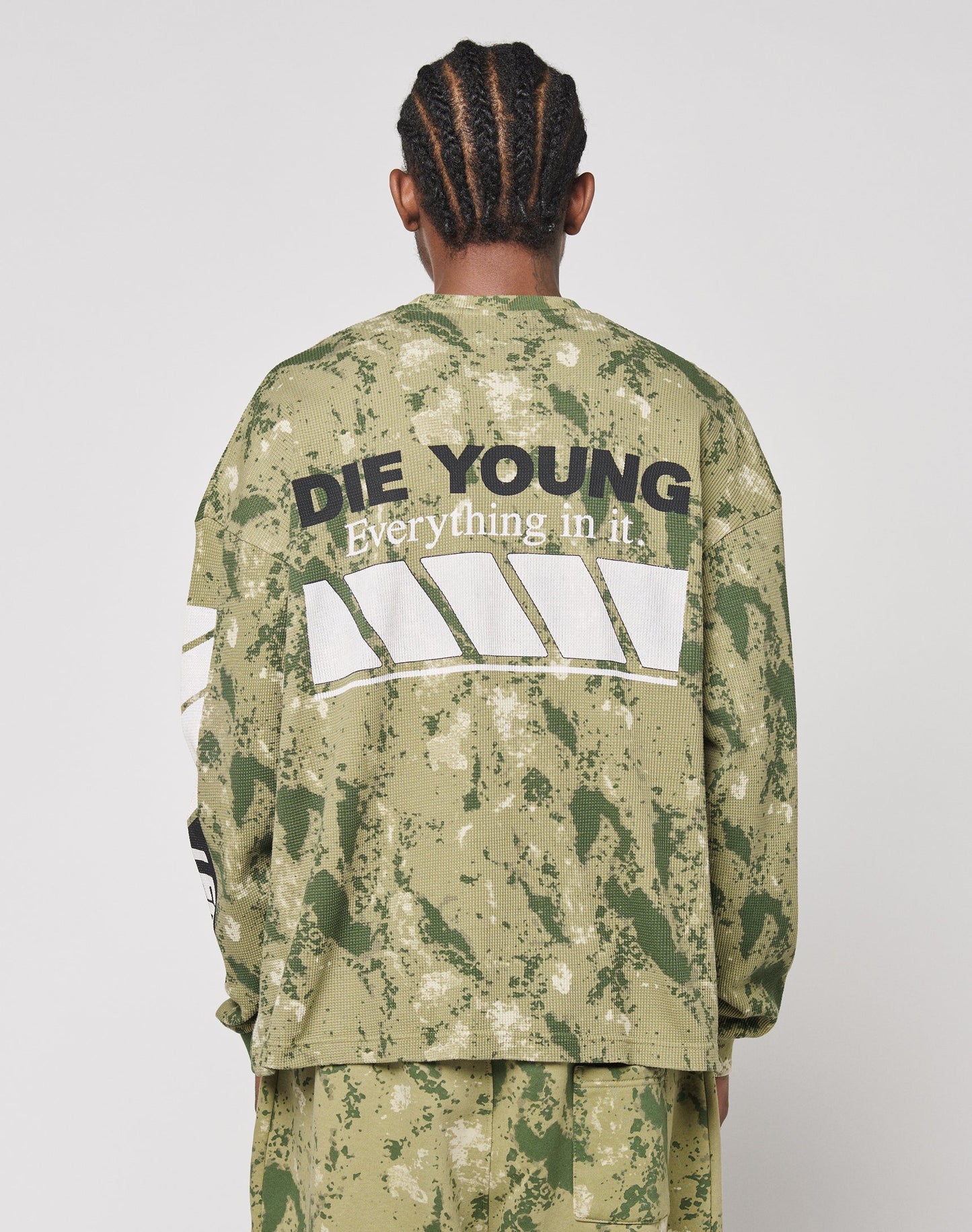 A person with braided hair, seen from behind, wears an oversize fit LFDY Racing Waffle Longsleeve by LIVE FAST DIE YOUNG. The back features DIE YOUNG Everything in it above diagonal white stripes.