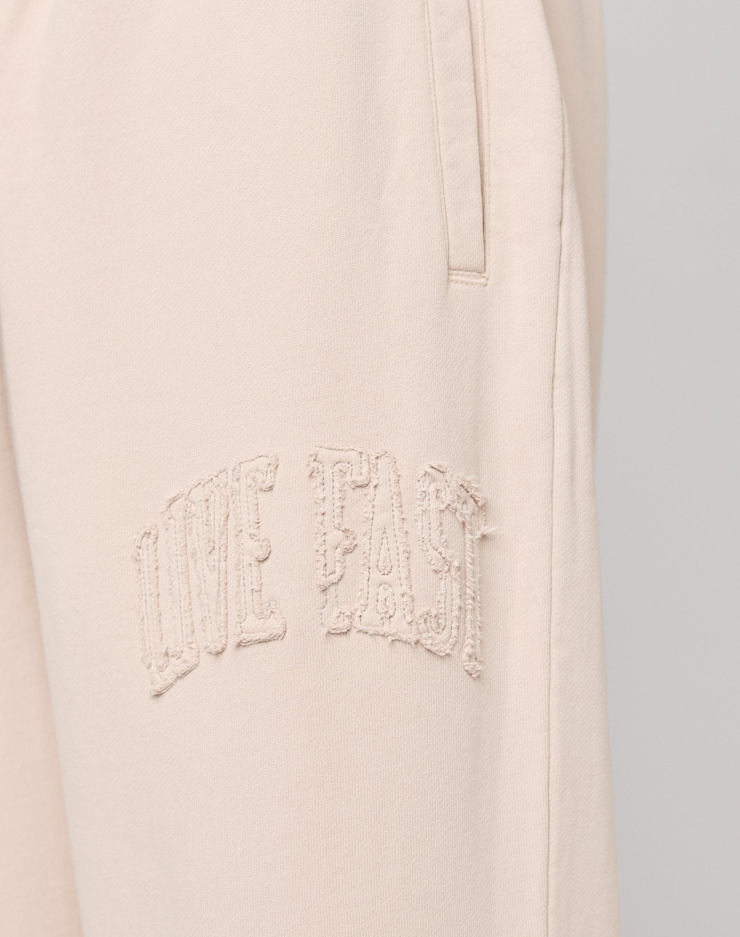 Close-up of Ripped College Wide Jogger by LIVE FAST DIE YOUNG in light beige, crafted from soft Baumwolle, with textured embroidered LIVE FAST text near the pocket.