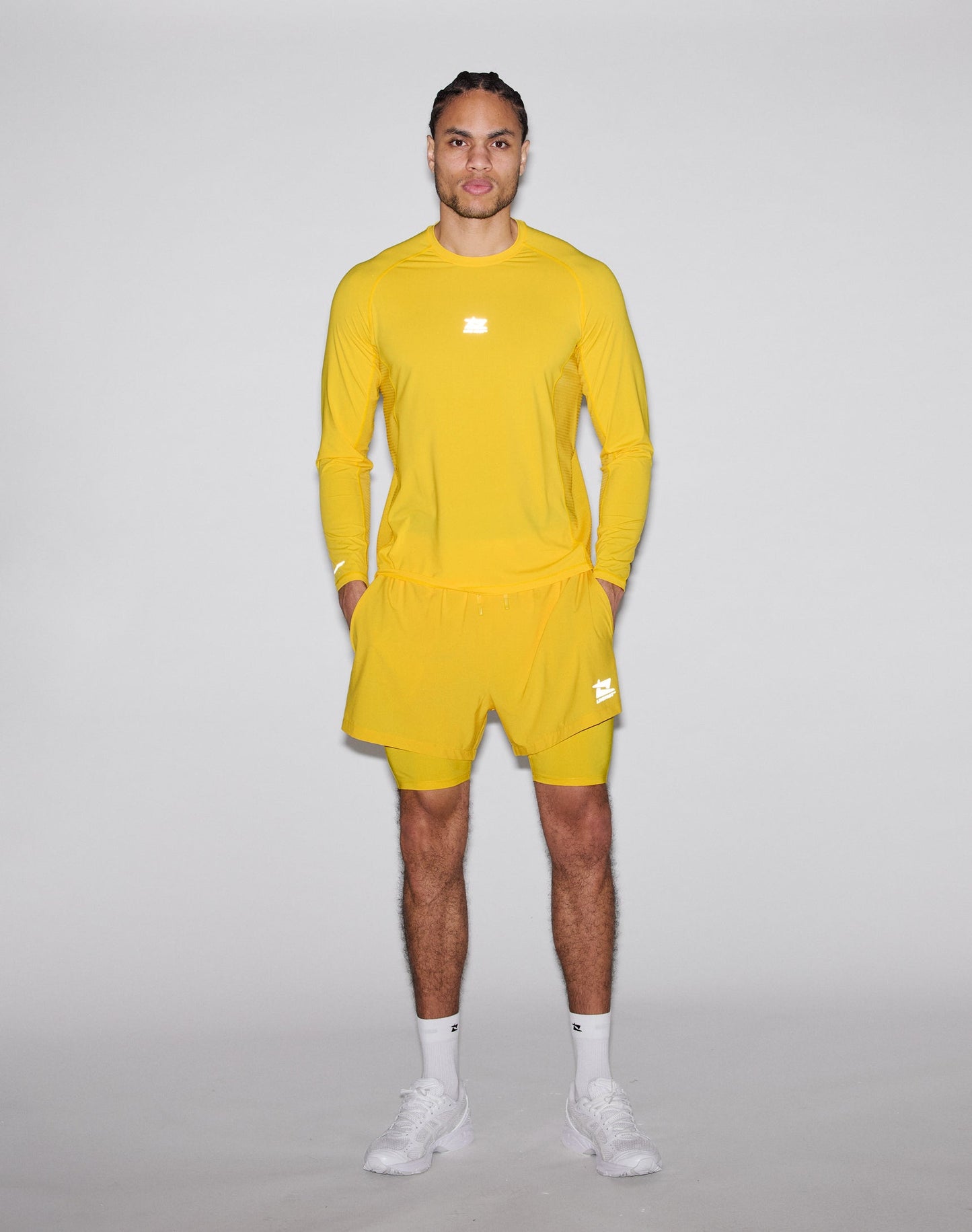 A person stands against a plain light gray background, wearing the LIVE FAST DIE YOUNG Live Fast Performance Longsleeve in bright yellow with matching shorts, white socks, and white sneakers.