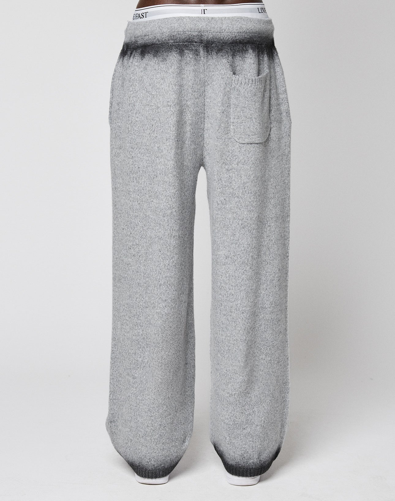 LIVE FAST DIE YOUNG’s Live Fast Boucle Pants feature a wide fit, straight leg, single front pocket, elastic waistband with text, and a gradient from dark to light gray at the waist and ankles. Displayed on a plain background.