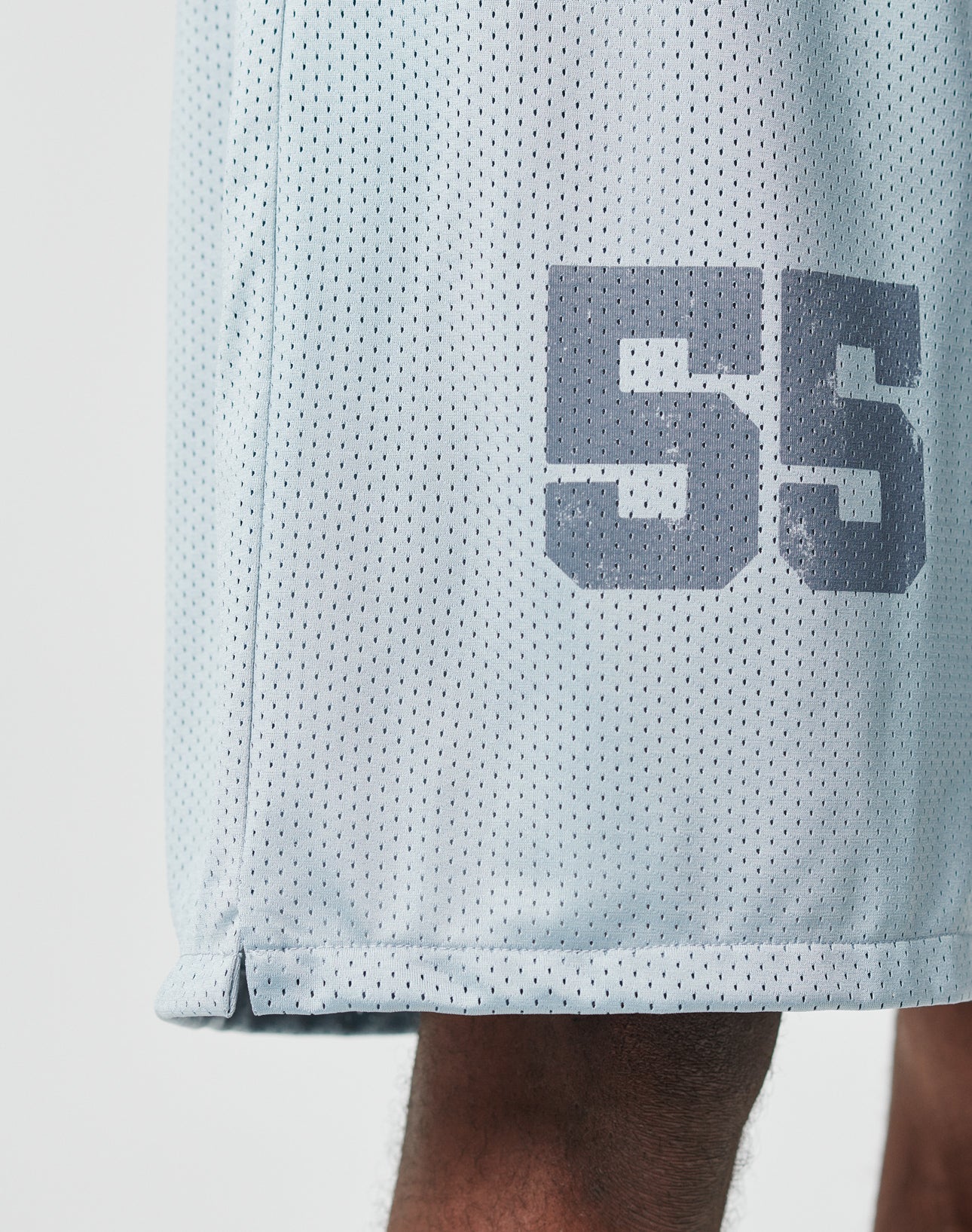 Close-up of a person wearing LIVE FAST DIE YOUNGs LFDY Loyal Shorts in light gray mesh with an elastic waistband and bold number 55 on the side. Only part of the leg and the oversized shorts are visible.