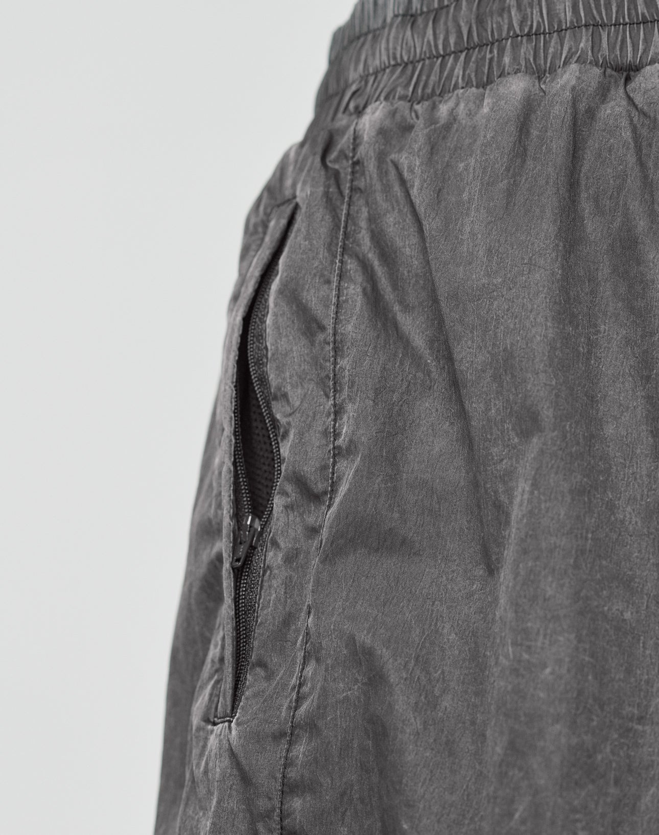 Close-up of LIVE FAST DIE YOUNG Live Fast Swimshorts in gray crinkled polyamide, Regular Fit, with elastic waistband and a side pocket with black zipper. Shown against a plain light background.