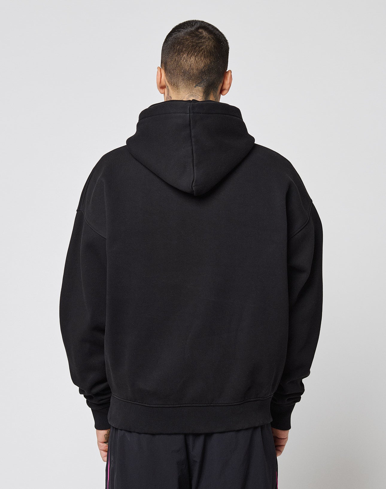 A person with short hair stands facing away from the camera, wearing a black LFDY Triple Racing Hooded by LIVE FAST DIE YOUNG and dark pants against a plain light gray background.