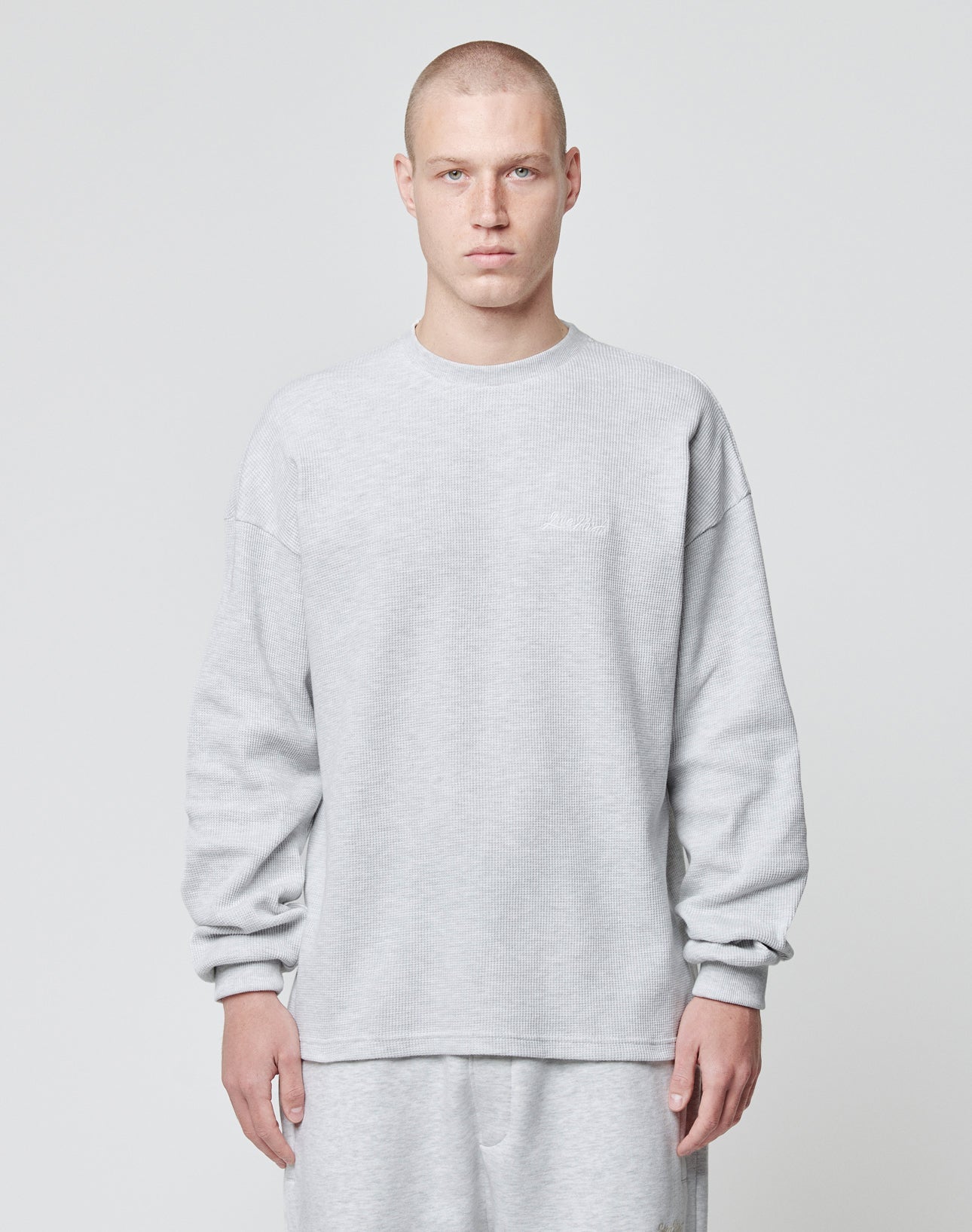 A person with a shaved head wears the LIVE FAST DIE YOUNG Basic Script Waffle Longsleeve in light gray with matching pants, standing against a plain light gray background and facing the camera with a neutral expression.