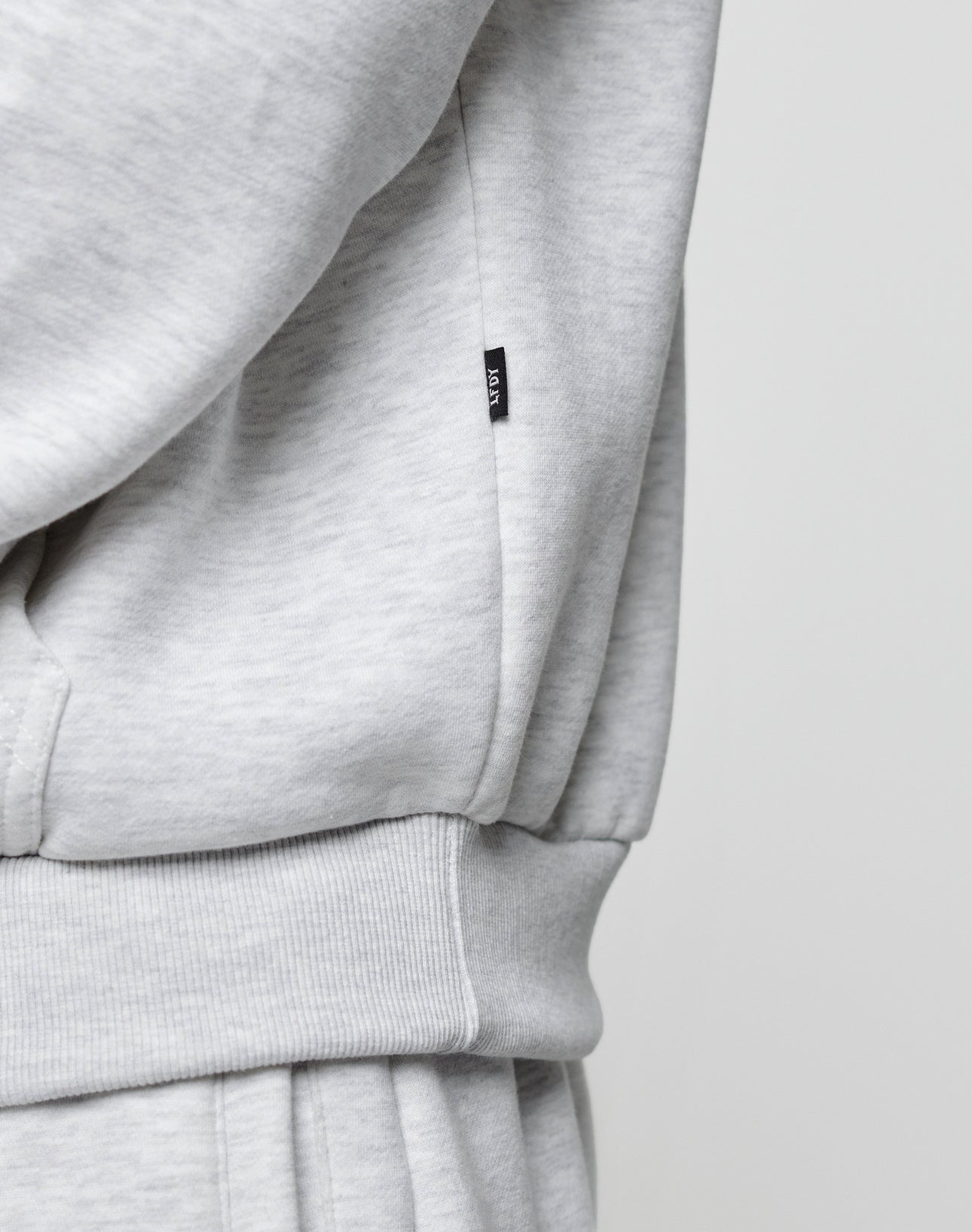 Close-up of the LIVE FAST DIE YOUNG Basic Blank Hooded in light grey, featuring an oversized fit, ribbed waistband, pocket, and a small black tag with white text. The soft cotton-polyester blend fabric and casual style are clearly visible.