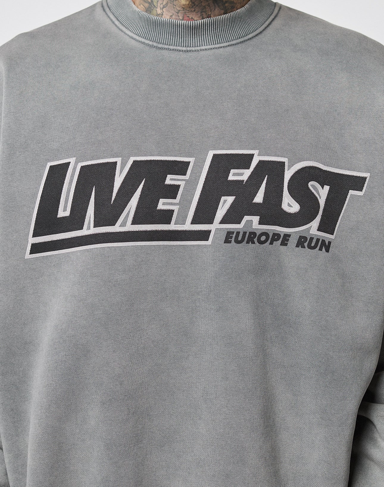 The LIVE FAST DIE YOUNG Live Fast Europe Run Sweater is a grey oversized sweatshirt with vintage wash, bold black LIVE FAST front print, and a smaller EUROPE RUN text across the chest.