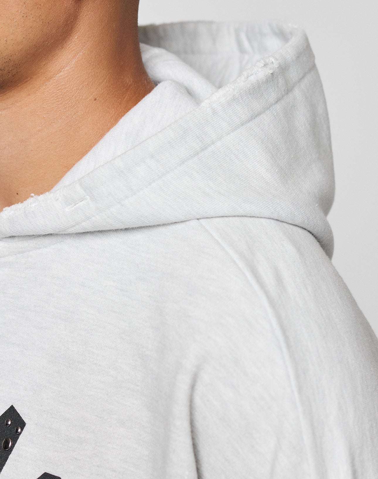 Close-up of a person wearing the LIVE FAST DIE YOUNG Live Fast Rivet Hooded Zip in light gray, highlighting the fabric texture and hood seam; only part of their face, neck, and shoulder are shown.