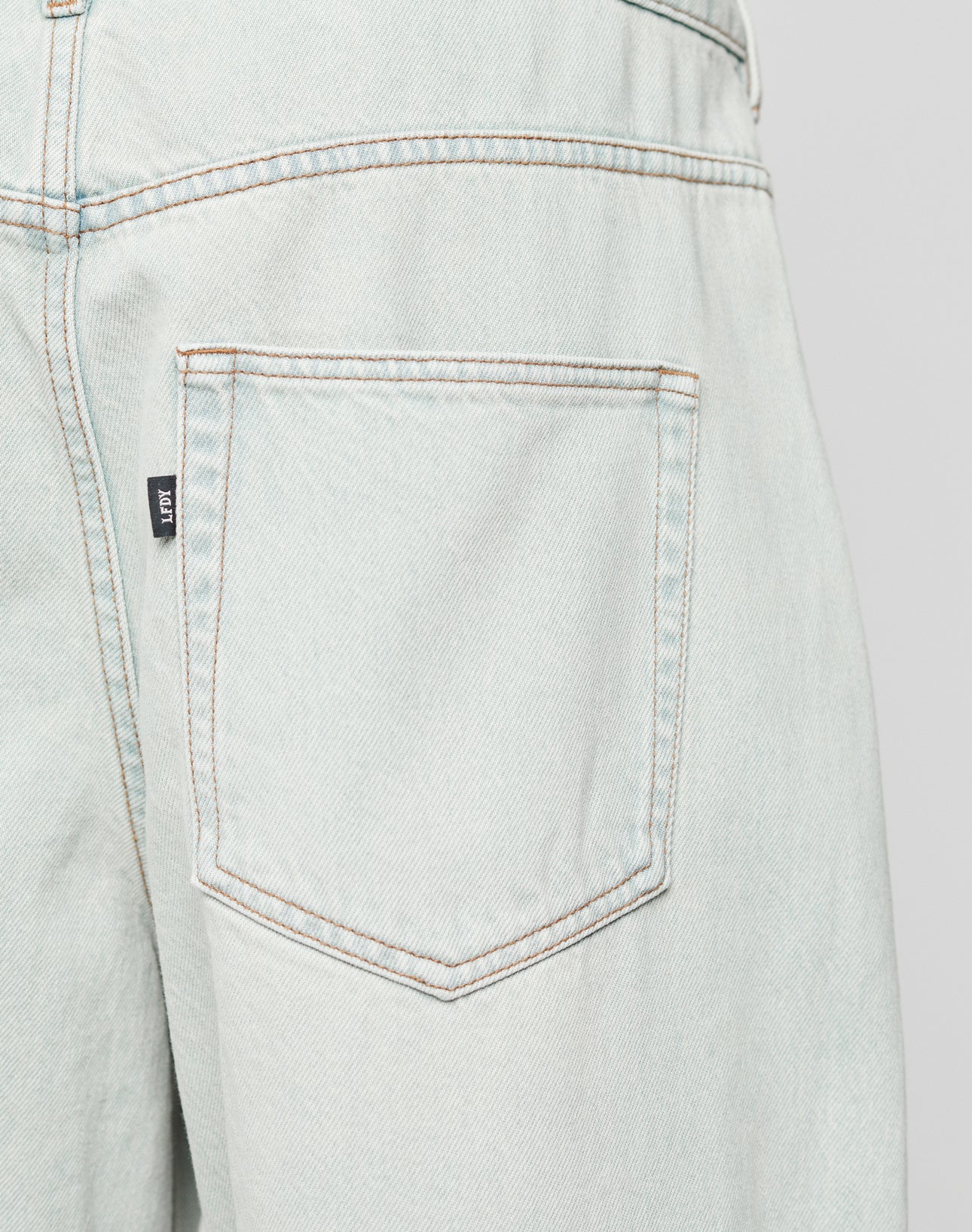 Close-up of the back pocket on LFDY Baggy Denim by LIVE FAST DIE YOUNG, showing a Flag-Label at the side seam, brown stitching, and slightly faded Baumwolle fabric for classic character.