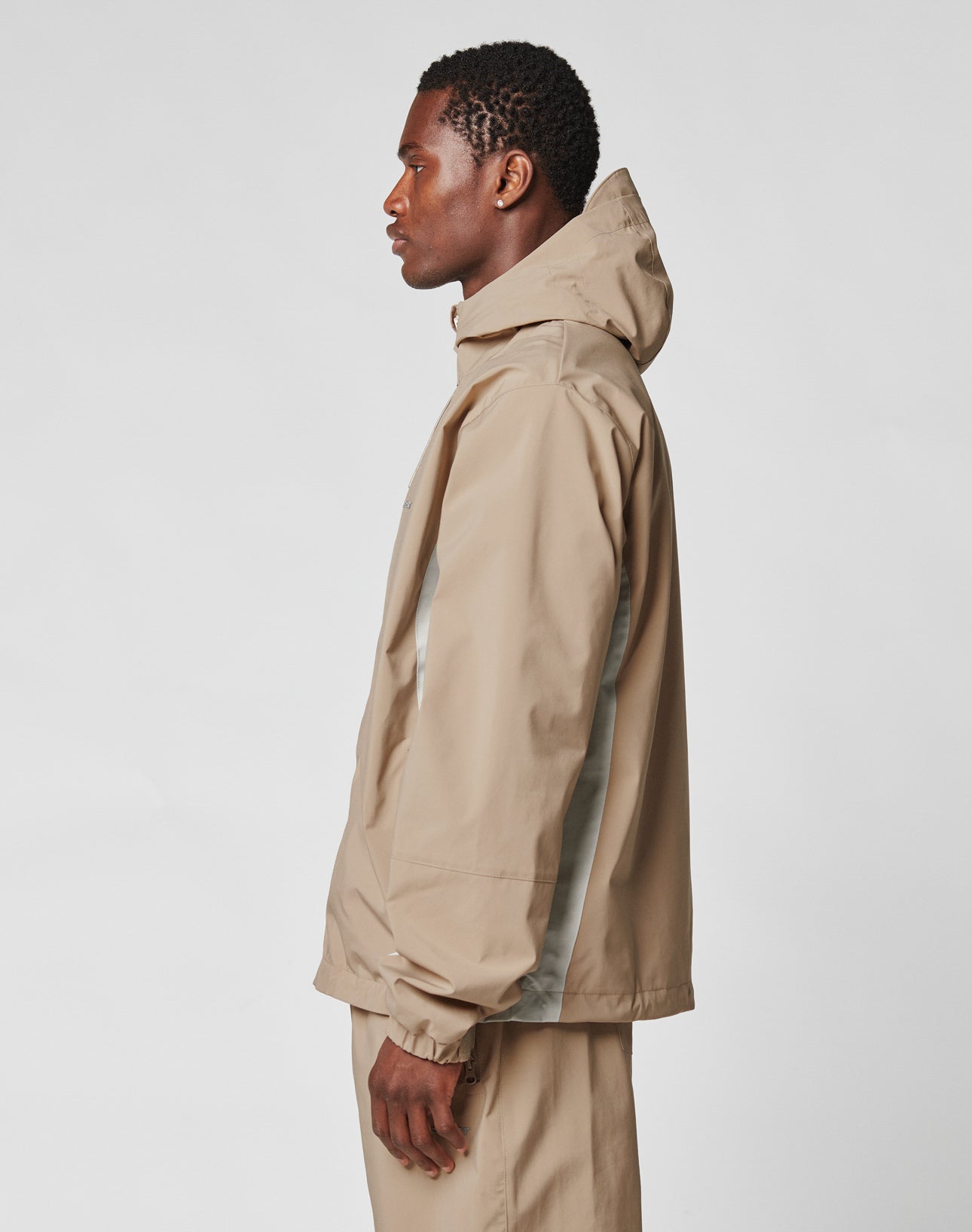 A man stands in profile wearing the LIVE FAST DIE YOUNG Basic Shell Jacket in an oversized fit with a wasserabweisender Reißverschluss and matching pants, set against a plain white background.
