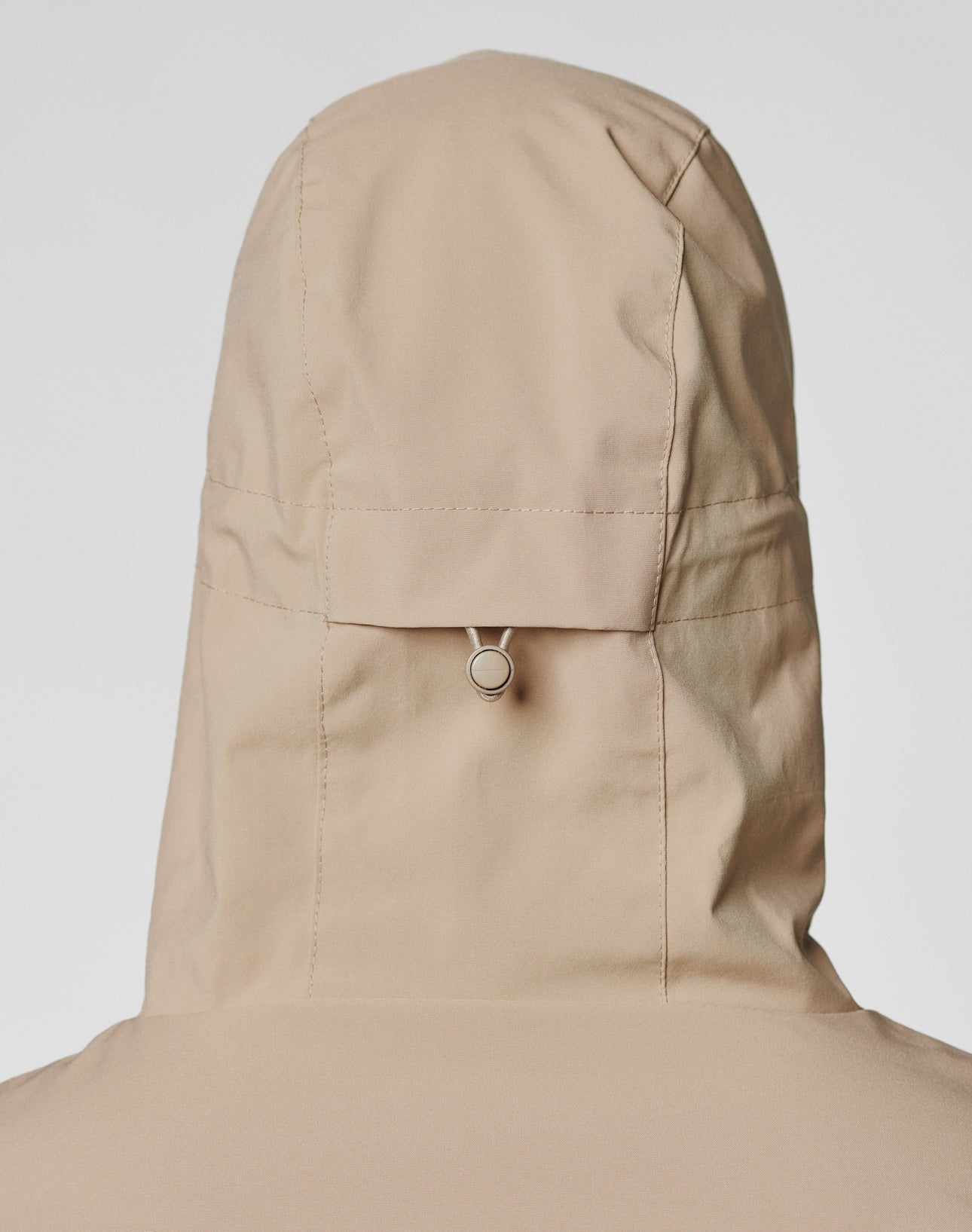 A close-up of the back of the beige LIVE FAST DIE YOUNG Basic Shell Jacket (Oversize Fit), featuring a silver ring pull tab on the hood, shown against a plain white background.