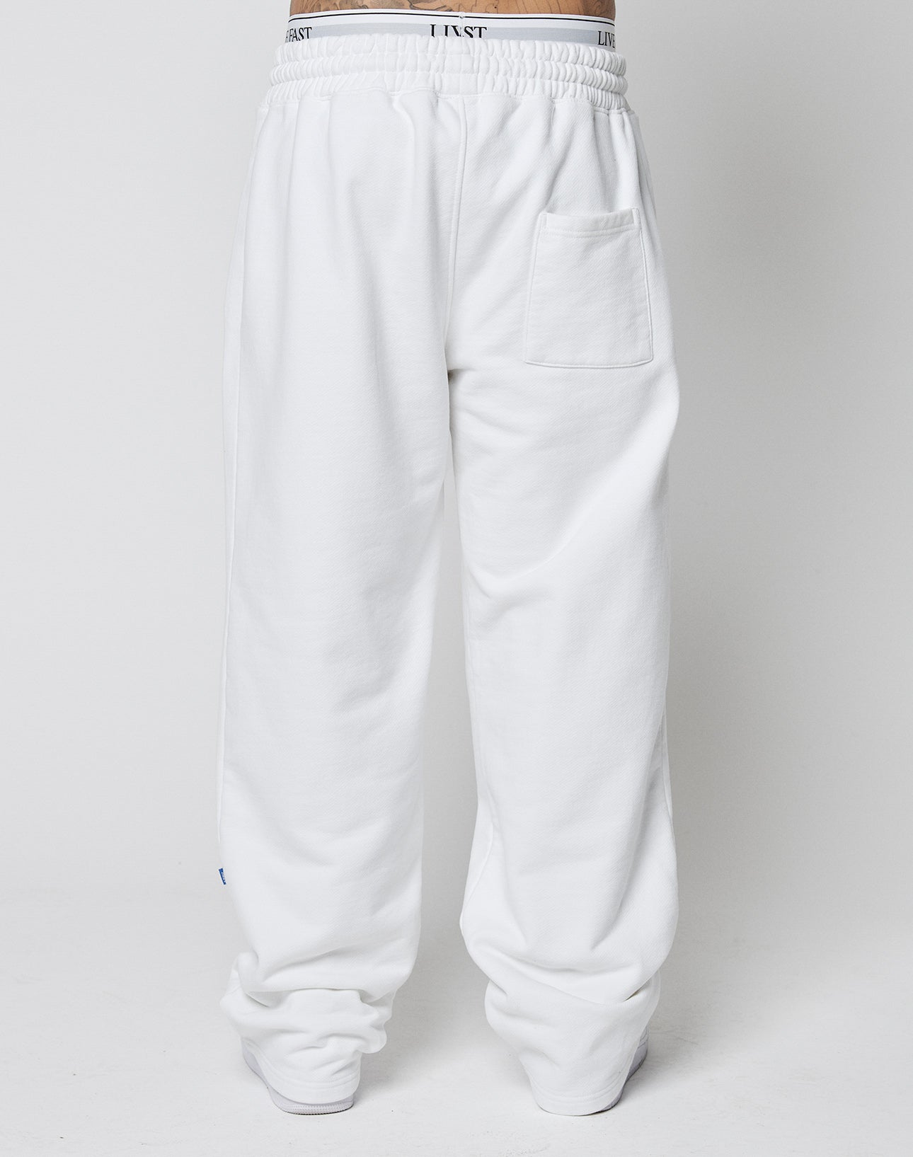 Model wears the LFDY Radiator Sweatpants by LIVE FAST DIE YOUNG—loose-fitting white pants with an elastic waistband, bold black text, and a single back pocket. The oversize fit creates a relaxed, modern look against a plain background.