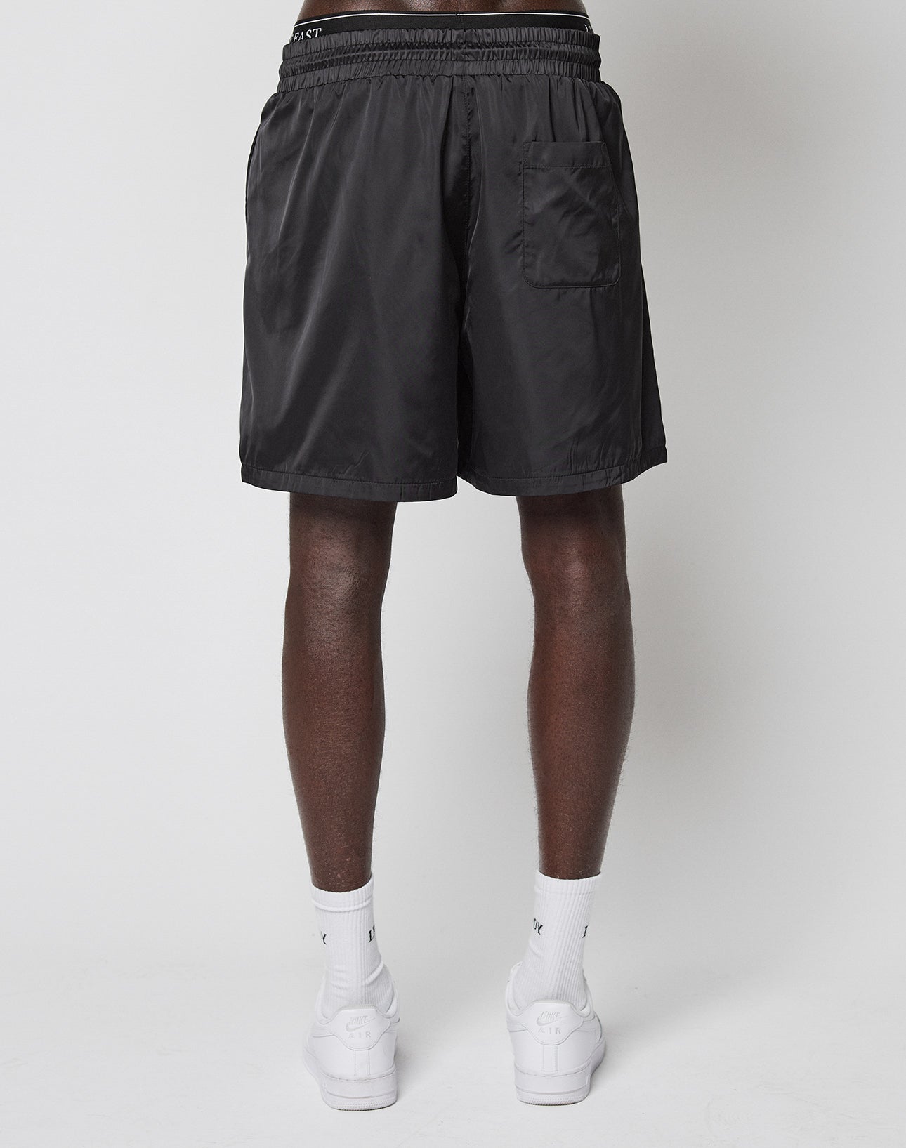 A person stands facing away, wearing LIVE FAST DIE YOUNG LFDY Retro Satin Shorts, white crew socks, and white sneakers against a plain light gray background.