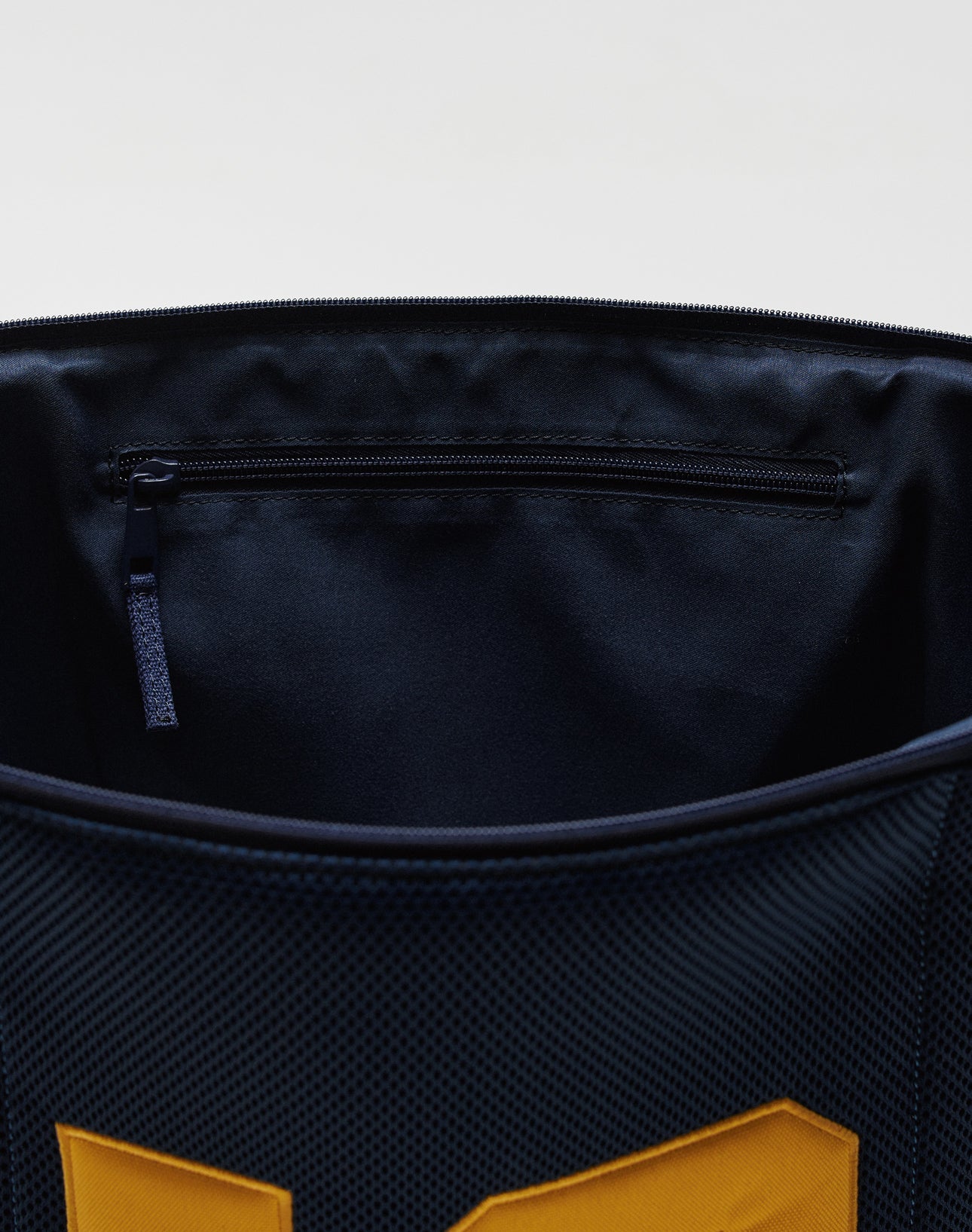 Close-up of the interior of the LFDY Mesh Beach Bag by LIVE FAST DIE YOUNG, featuring a zippered pocket with mesh detail and distinctive yellow accents on its dark blue exterior.