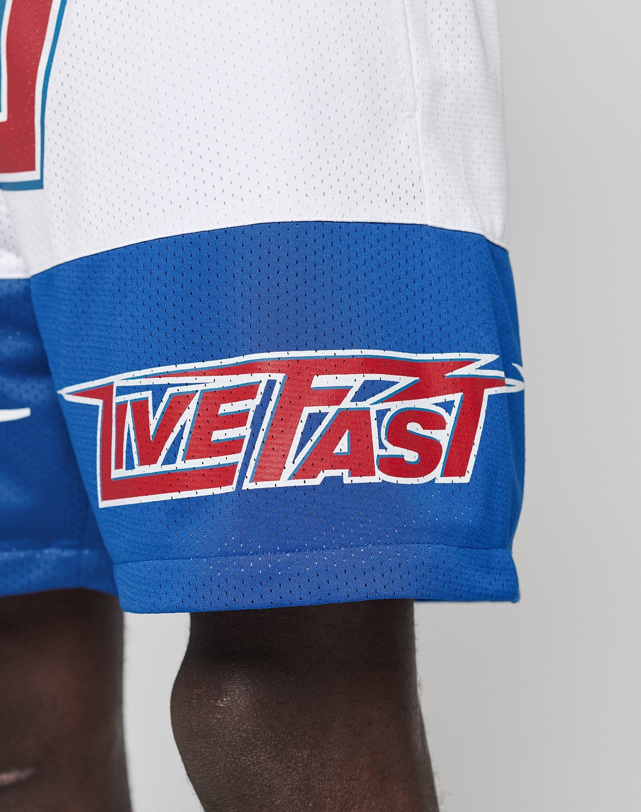 A close-up of LFDY Racing Mesh Shorts by LIVE FAST DIE YOUNG, made from blue and white polyester, featuring bold red and white LIVE FAST prints on the lower left leg against a plain background.