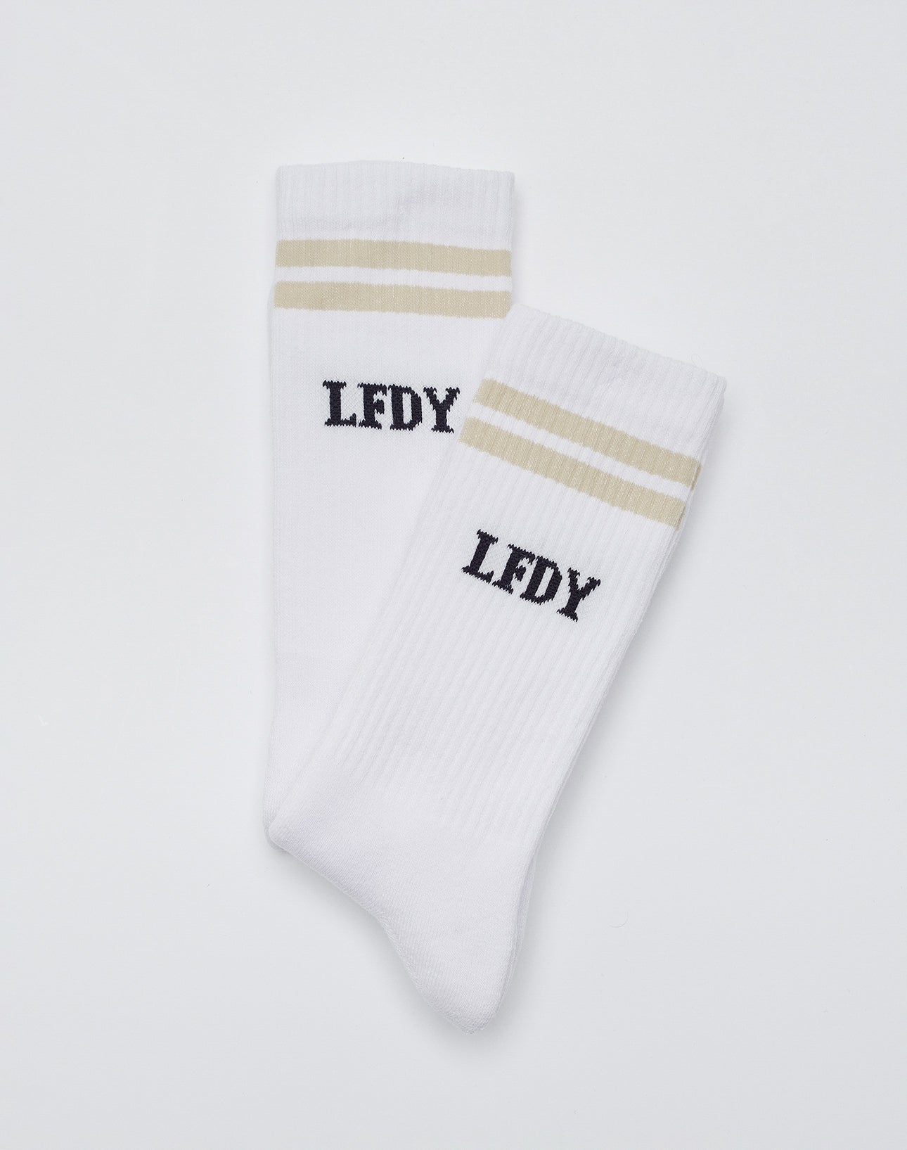 The Basic Socks (2 Pack) by LIVE FAST DIE YOUNG are white crew socks with two beige stripes and black LFDY text, crafted from a soft cotton blend with polyamide and elastane for comfort and stretch, shown on a plain white background.