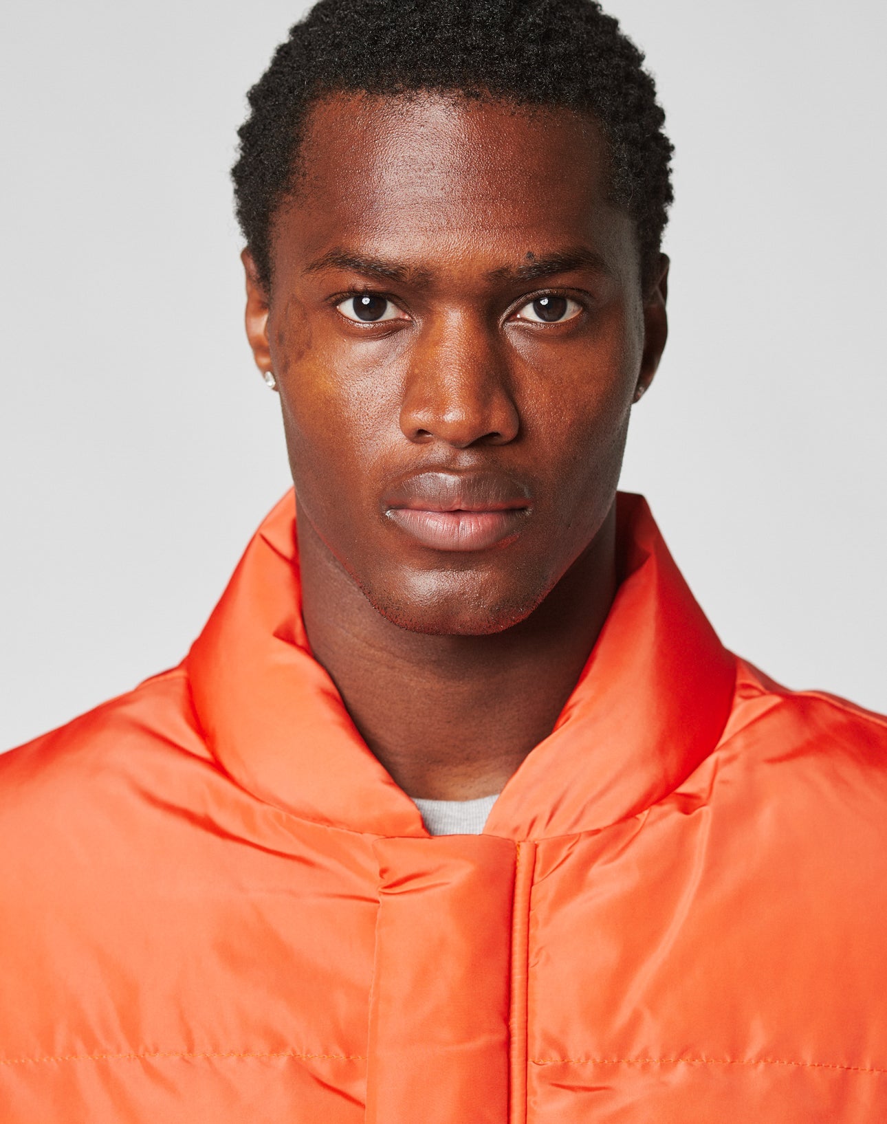 A man with short curly hair wears the LIVE FAST DIE YOUNG Live Fast Cropped Vest featuring large patch pockets and elastic drawcords, staring directly at the camera against a plain background.