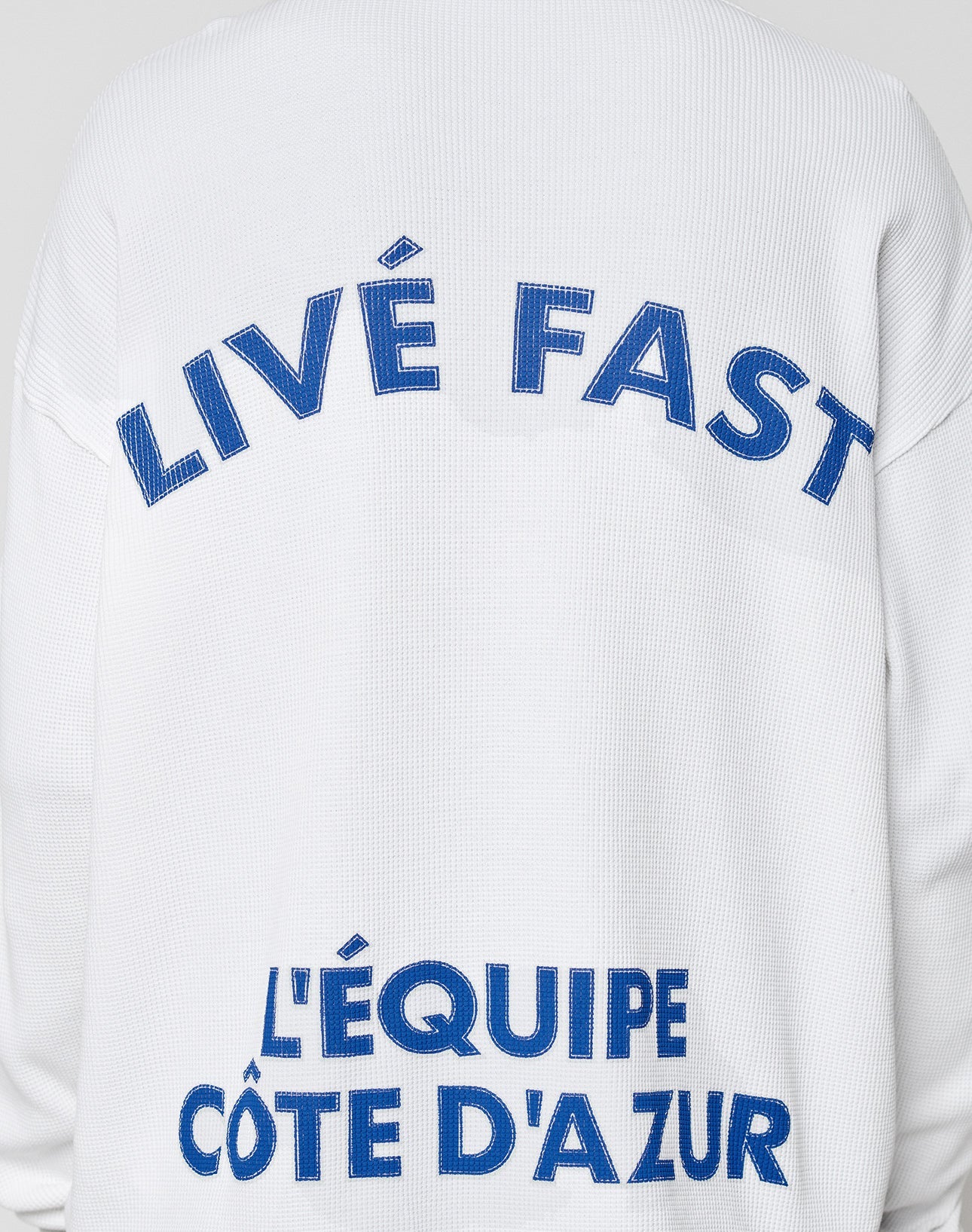 The LÉquipe Waffle Longsleeve by LIVE FAST DIE YOUNG is a white, textured oversize fit shirt in 100% cotton, featuring a bold blue LIVE FAST backprint above LÉQUIPE CÔTE DAZUR.